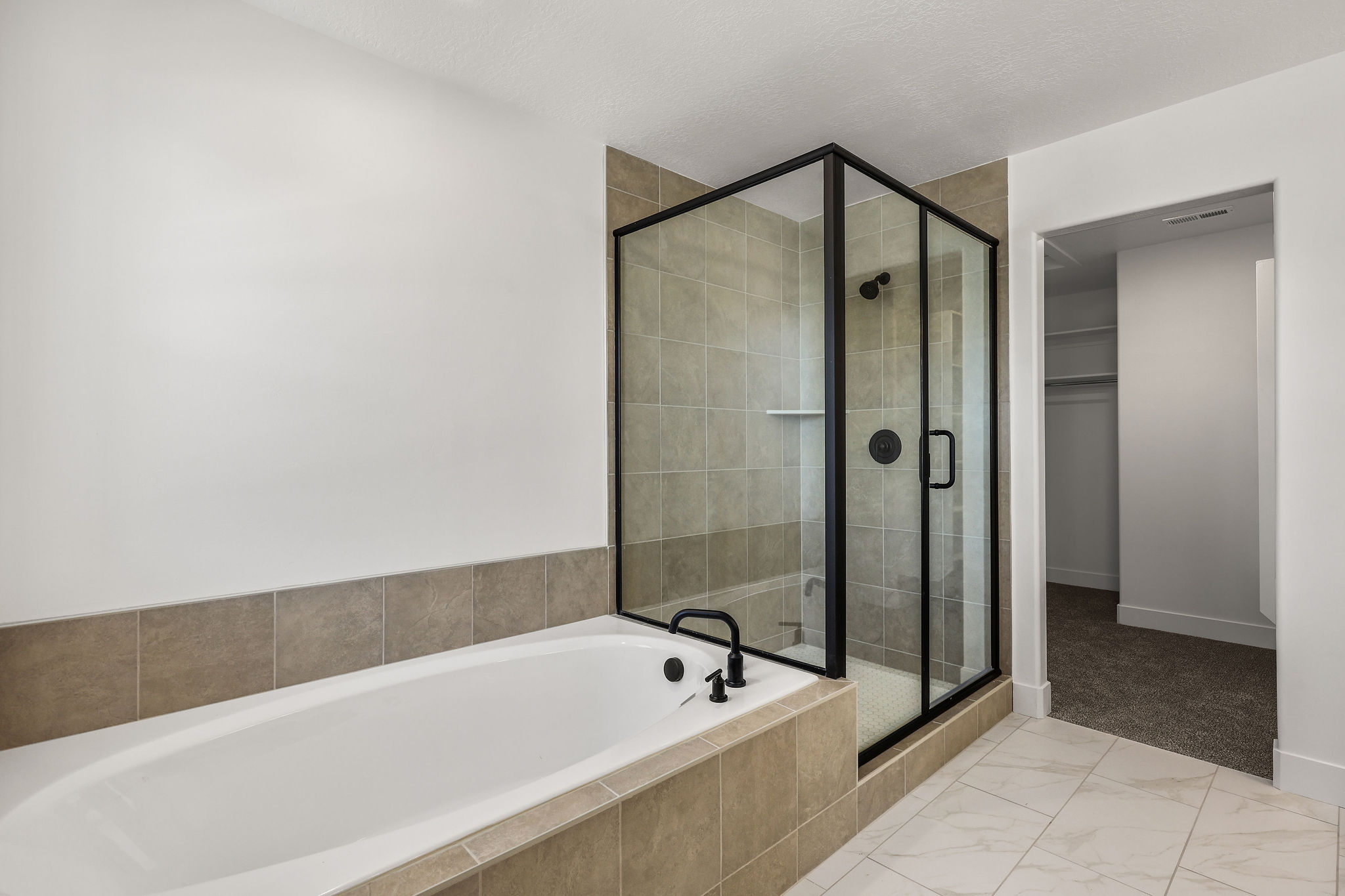 Bathroom featuring a built-in tub with matte black fixtures, a tiled surround, and a glass-enclosed shower with matte black trim