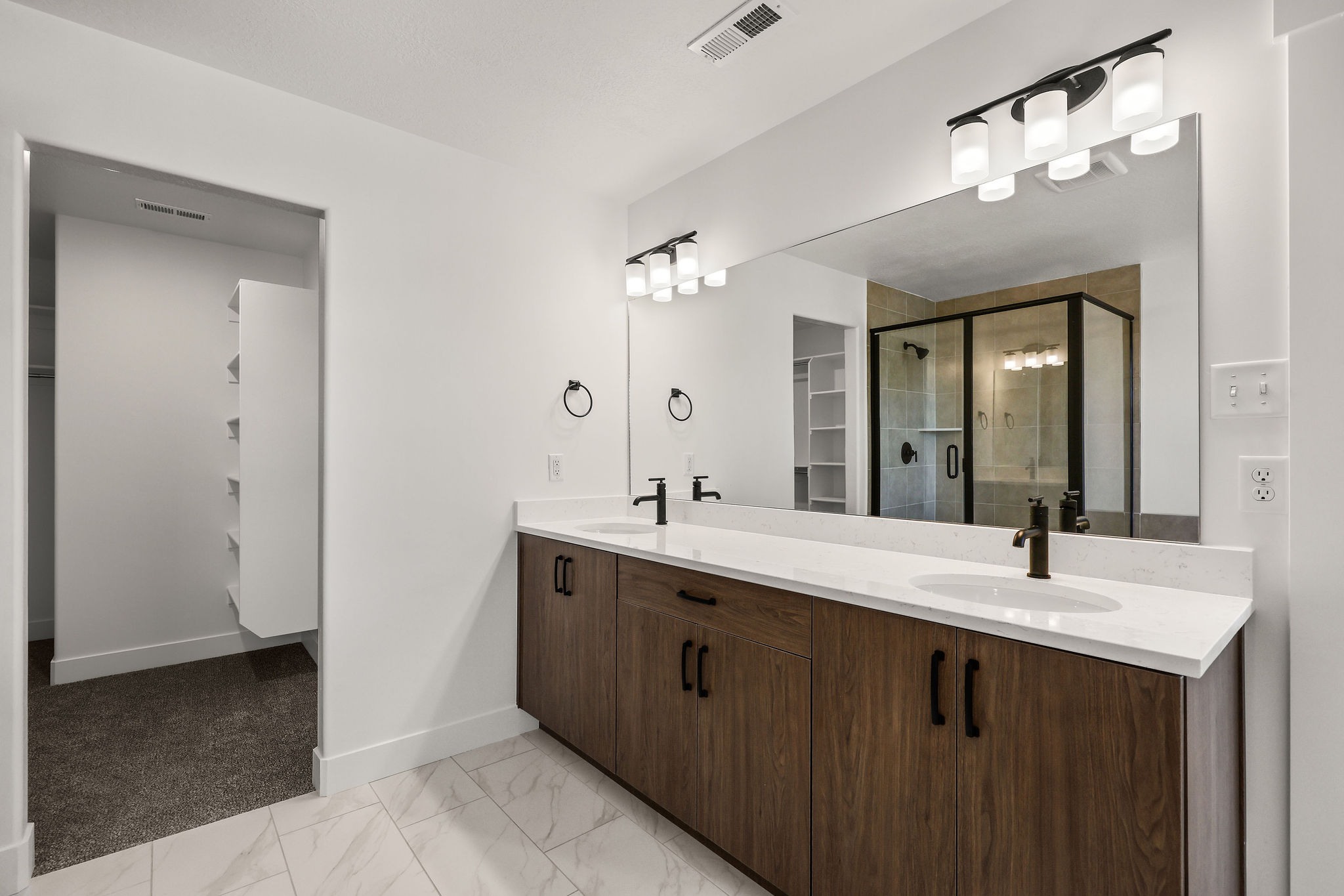 Bathroom featuring a dual-sink vanity with wood-finish cabinetry, white countertops, and matte black fixtures