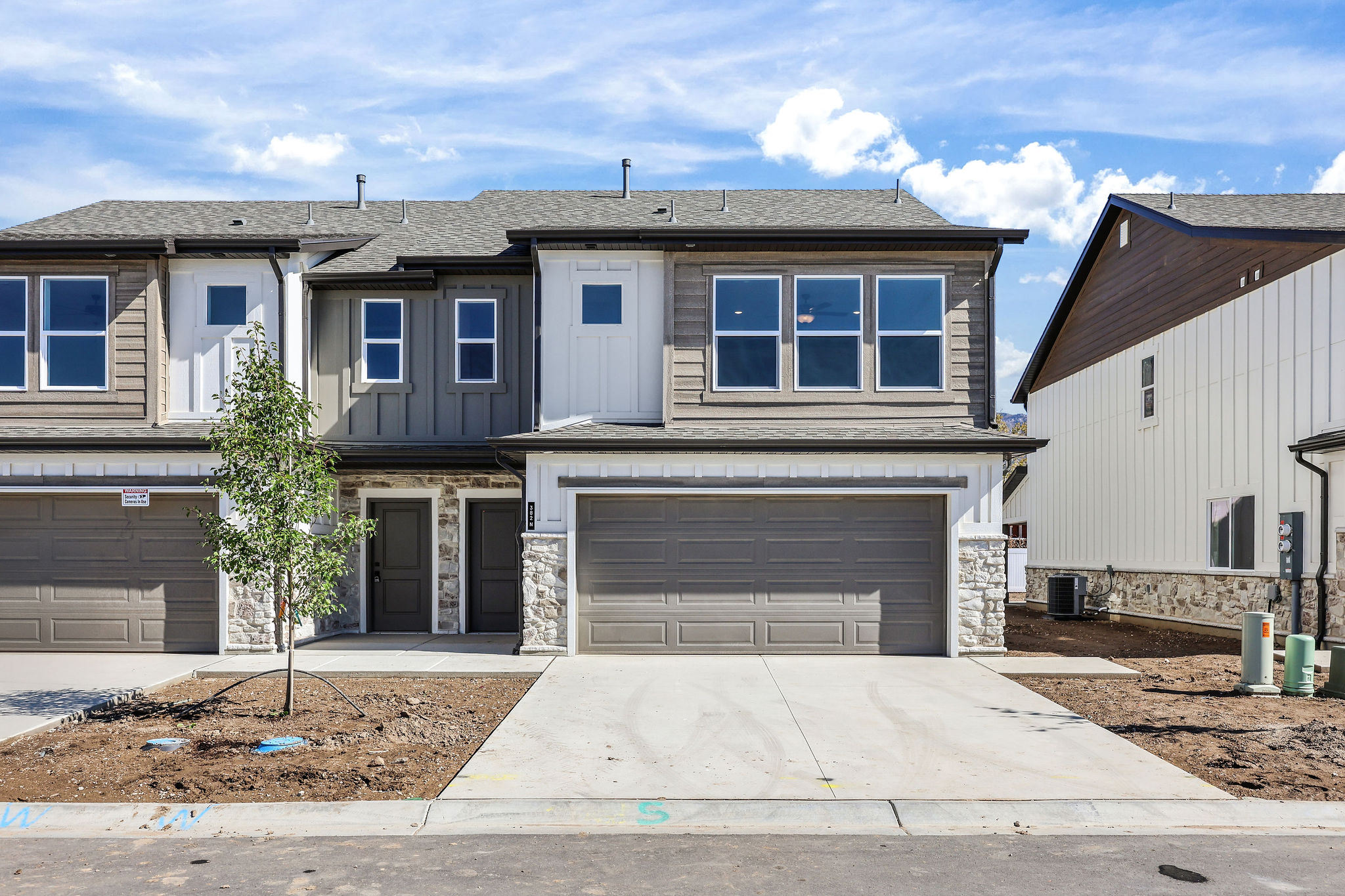 Modern townhome exterior featuring an attached two-car garage, concrete driveway, and stone veneer accents