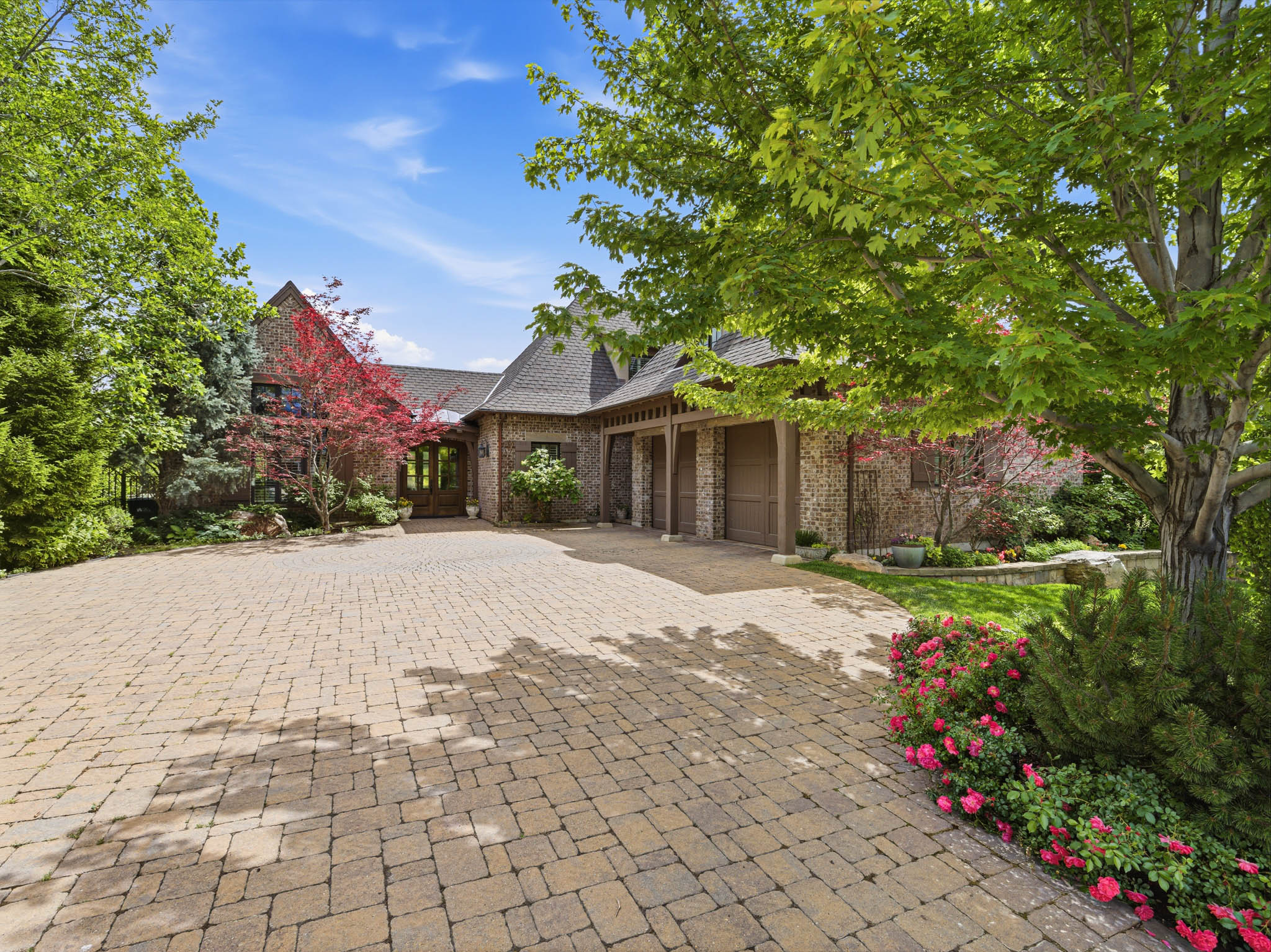 Brick exterior residence featuring a multi-car garage, pitched roofline, and a substantial paver driveway
