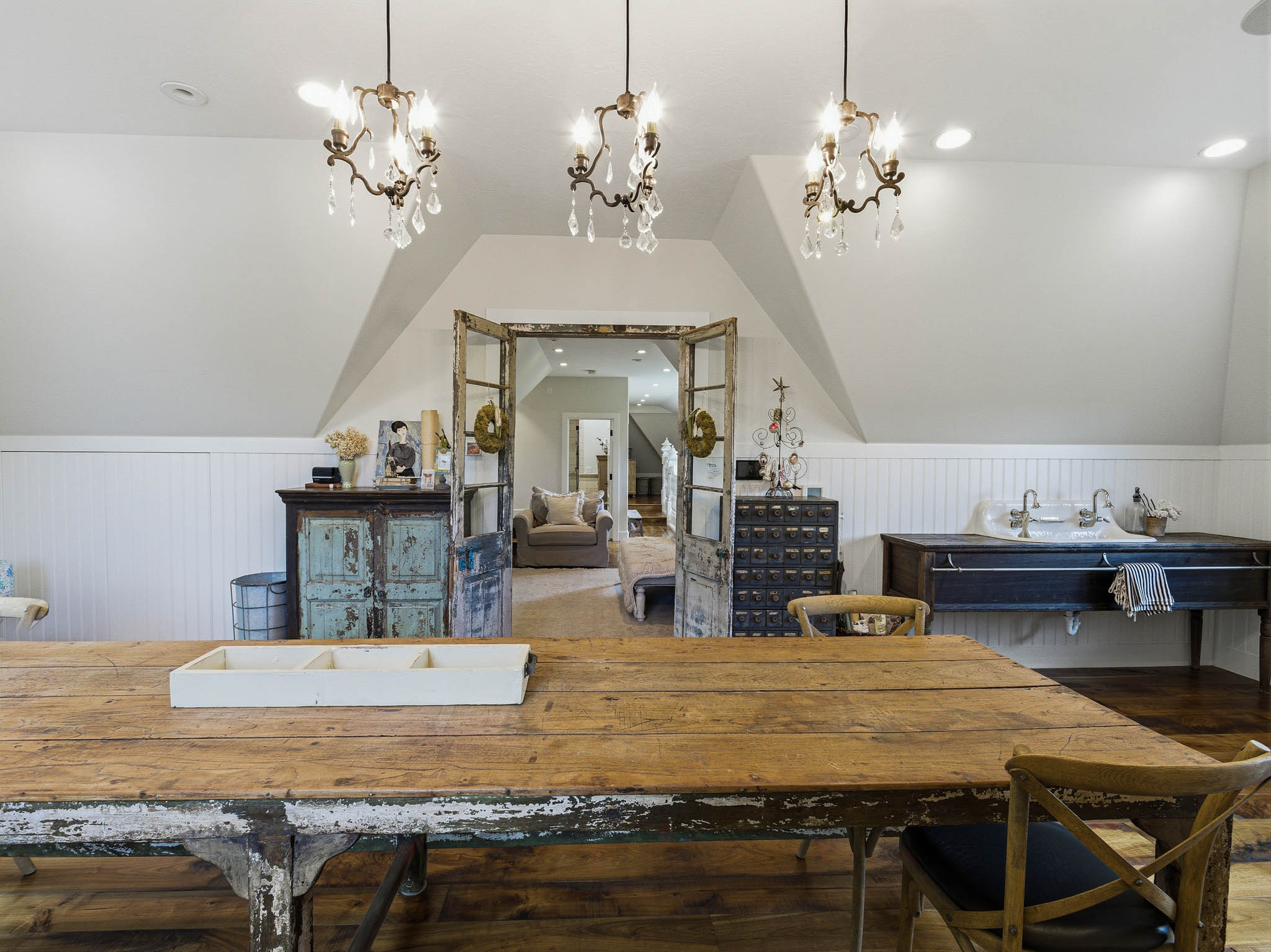 Attic living area featuring three crystal-accented chandeliers, wood-finish flooring, and white paneled wainscoting