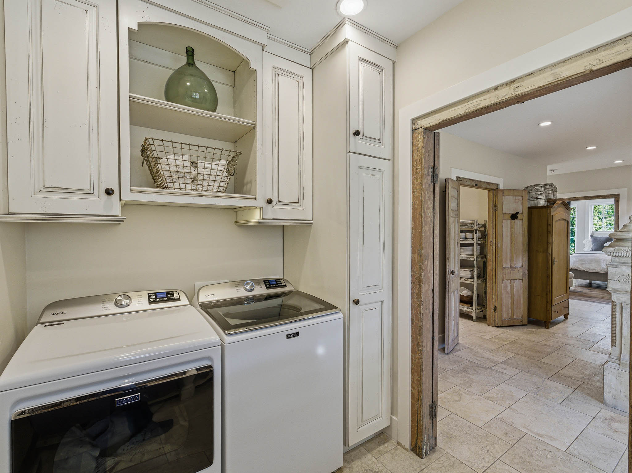 Dedicated utility area featuring distressed white cabinetry with integrated shelving and tall storage, tile flooring, and a wide entryway