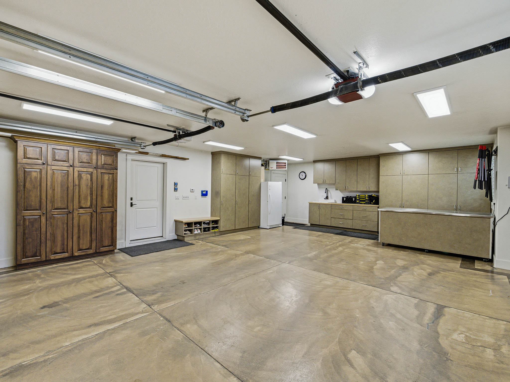 Spacious garage featuring a durable concrete floor, extensive built-in cabinetry, overhead lighting fixtures, and a white entry door