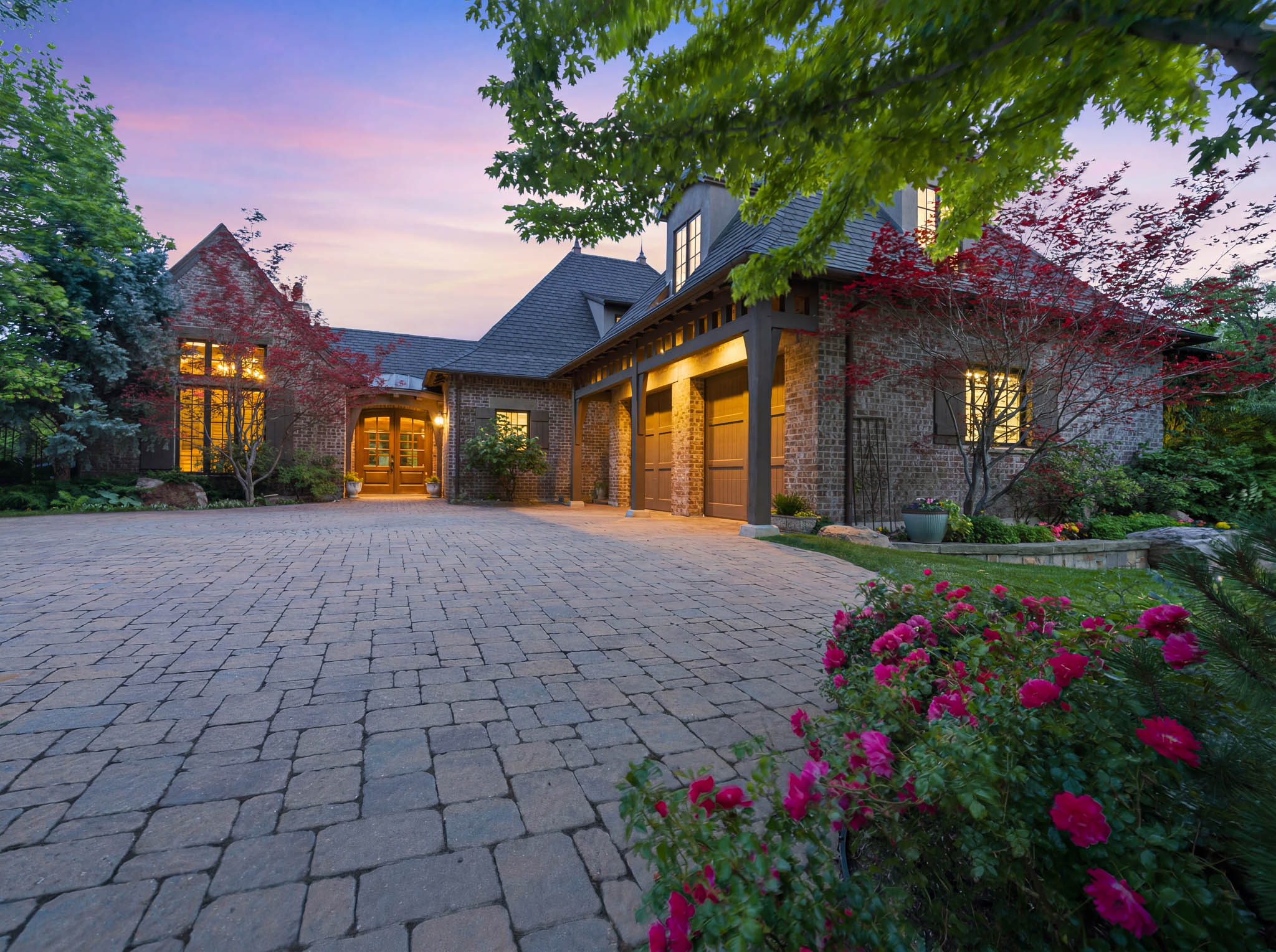 Stone and brick exterior residence featuring a paver driveway, multiple dormer windows, and a three-car garage