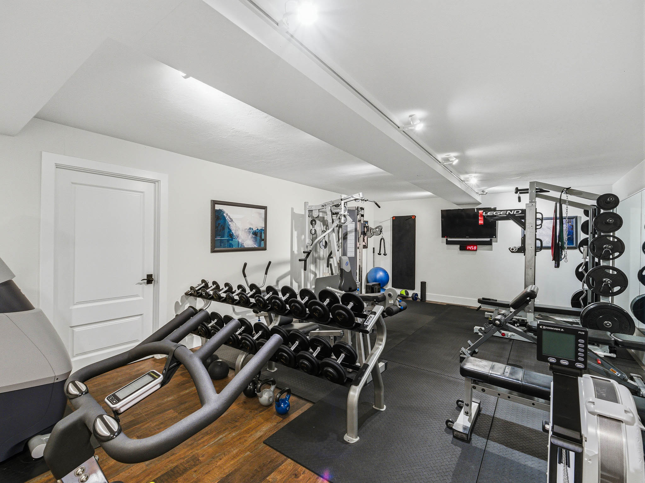 Dedicated fitness space featuring rubberized flooring and a wood-finish flooring section, recessed lighting, and a mounted flat-screen display
