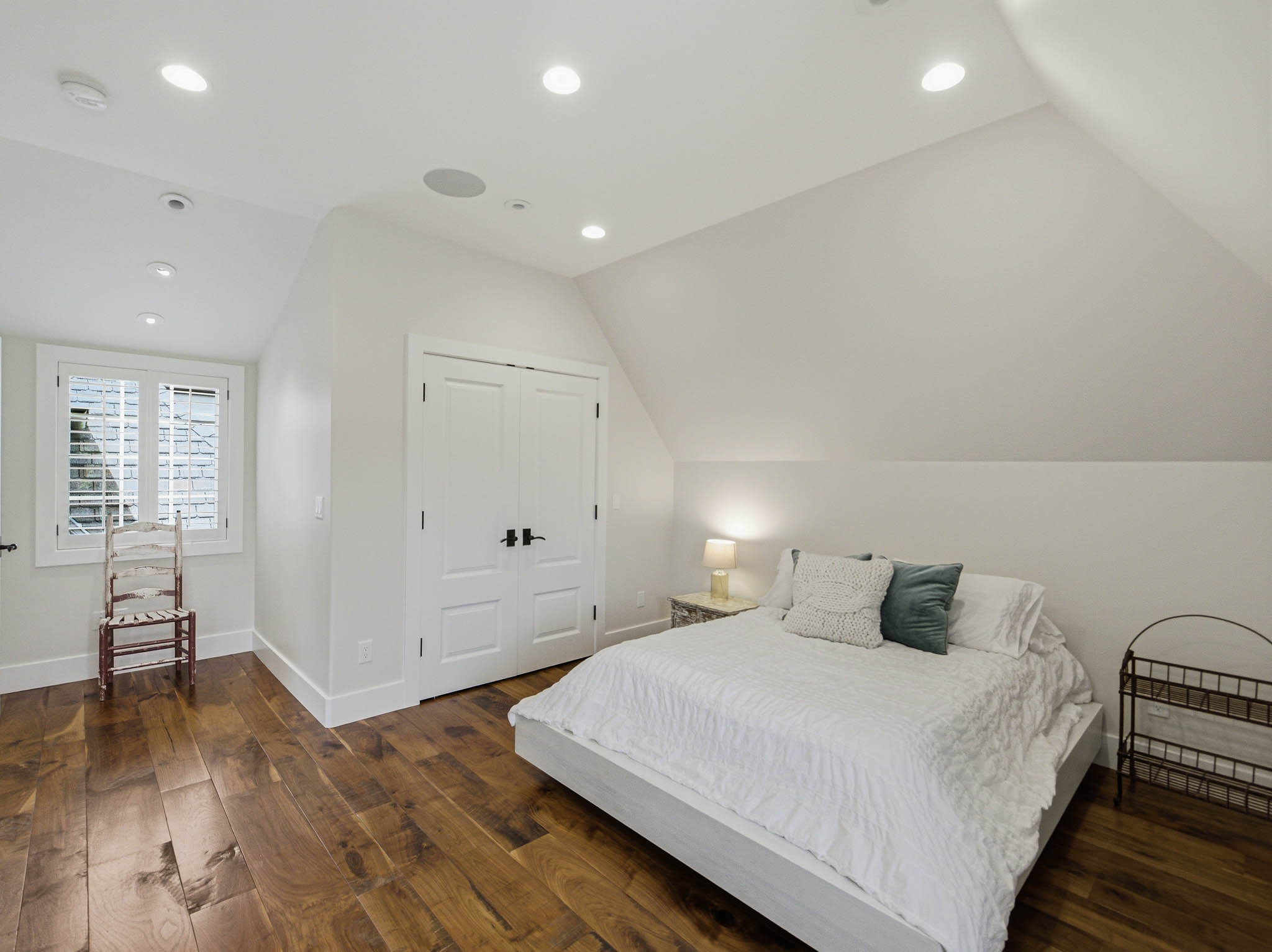Attic room featuring wood-finish flooring, recessed lighting, white double doors with matte black hardware, and a window with plantation shutters