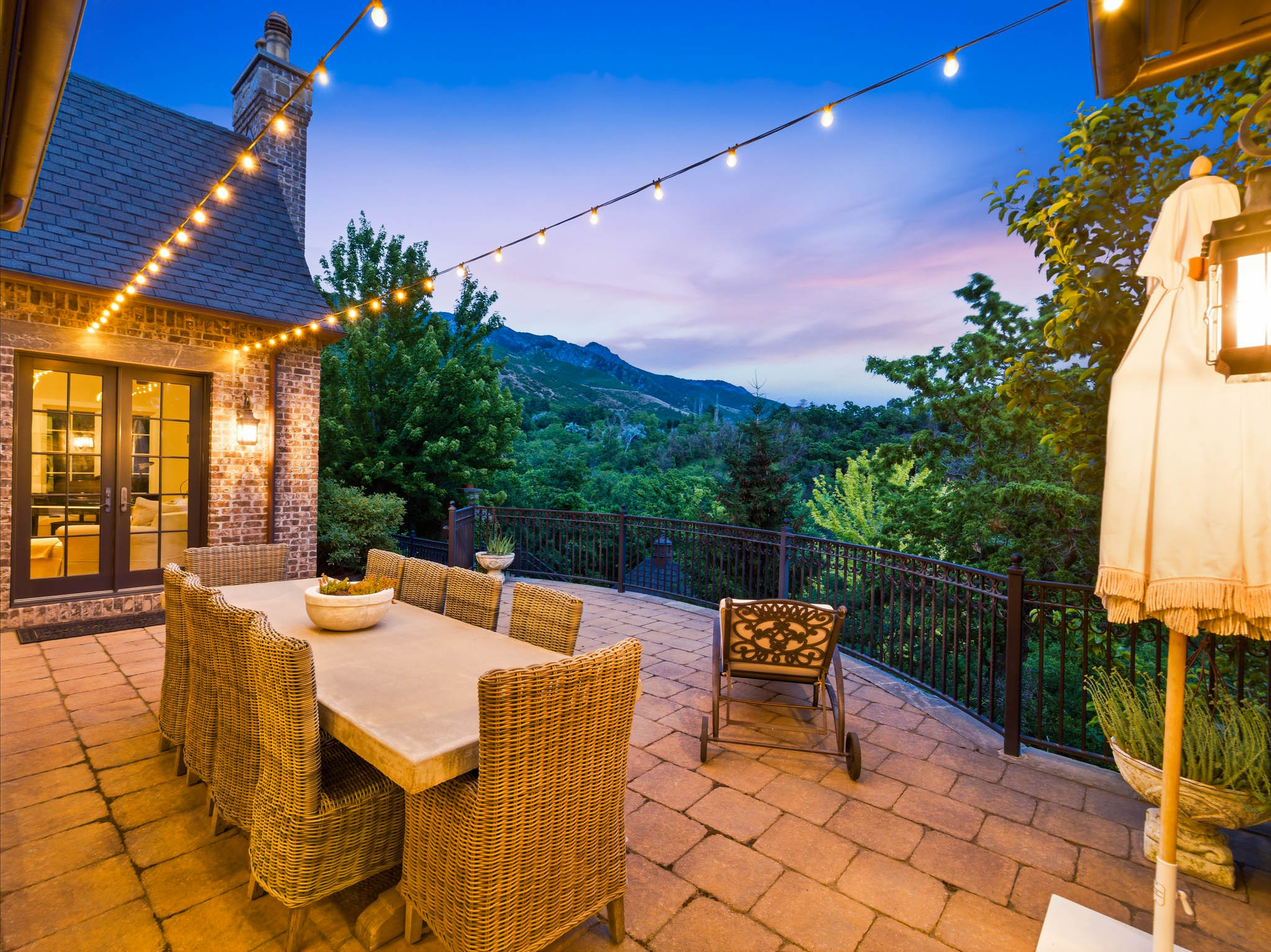 Expansive paver patio featuring a wrought iron railing, string lighting, and direct access to interior spaces through French doors