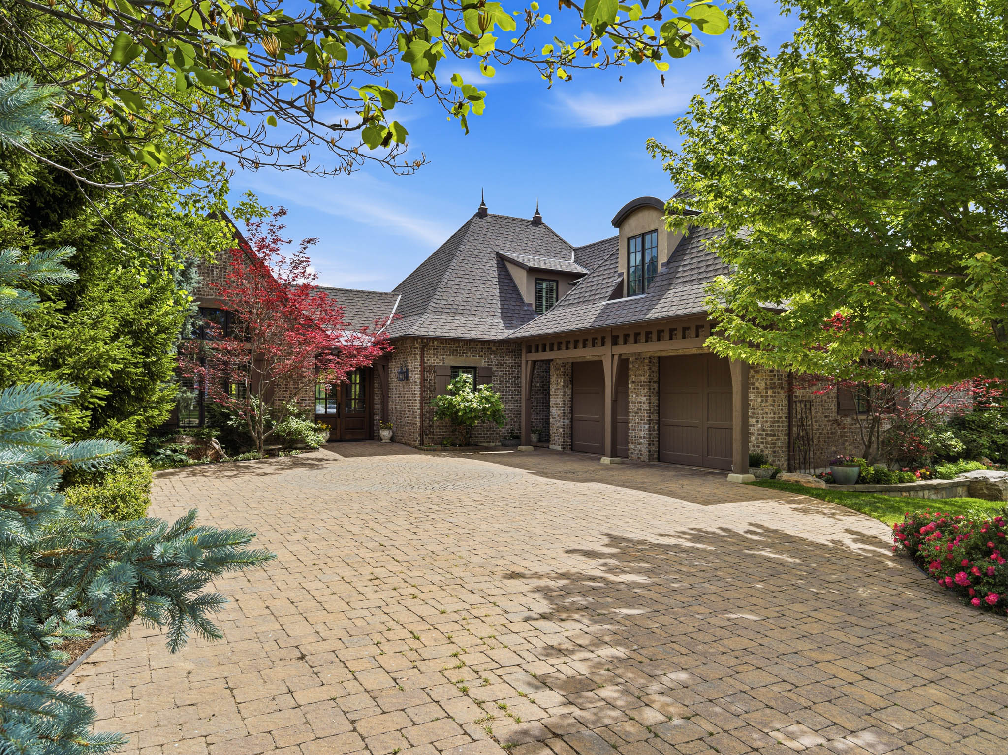 Stone paver driveway leading to a brick and stone exterior residence with a multi-gabled roofline