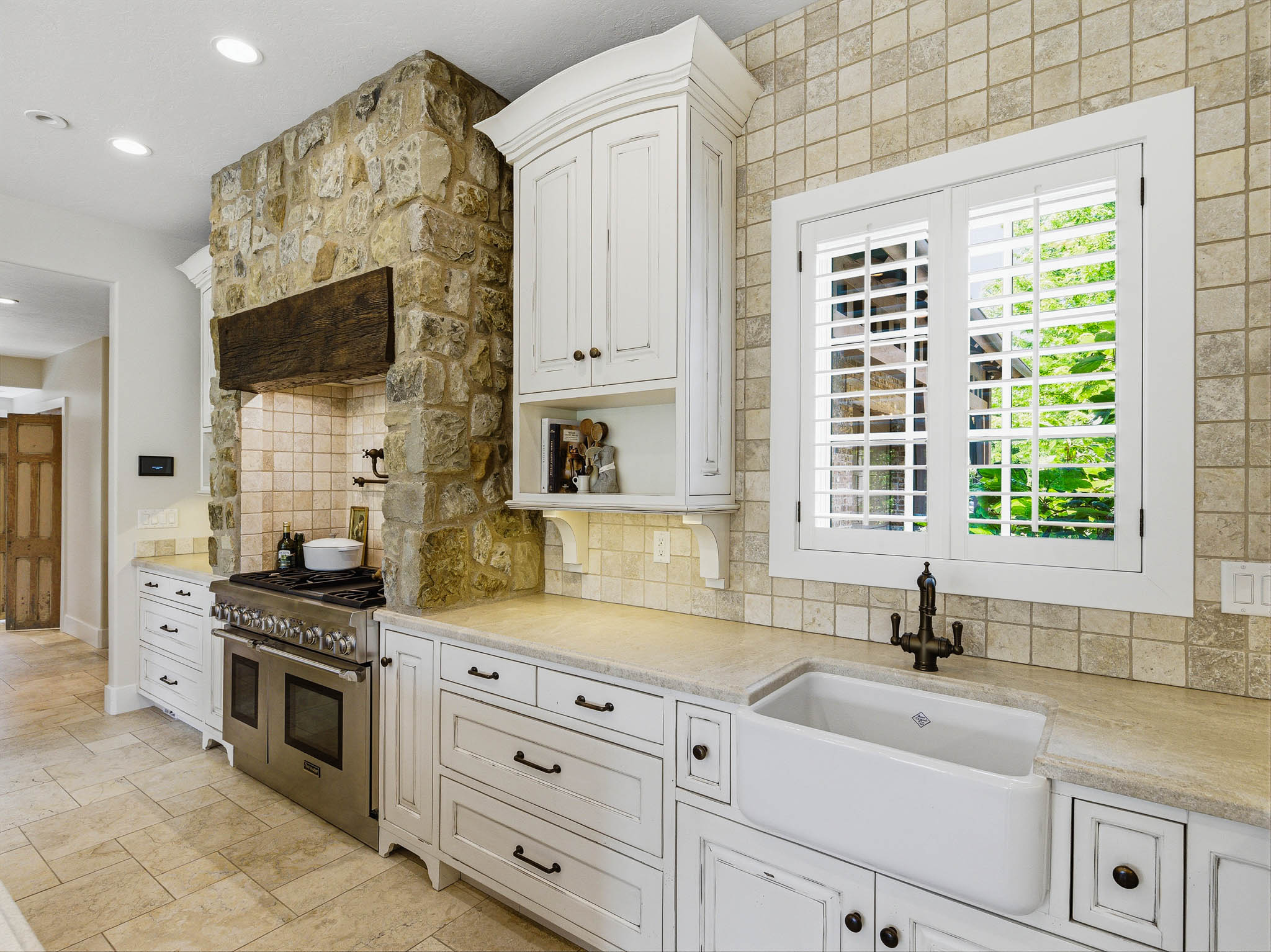 Kitchen featuring a stone range hood, stainless steel professional-style range, farmhouse sink, white cabinetry with dark hardware, and a tiled backsplash