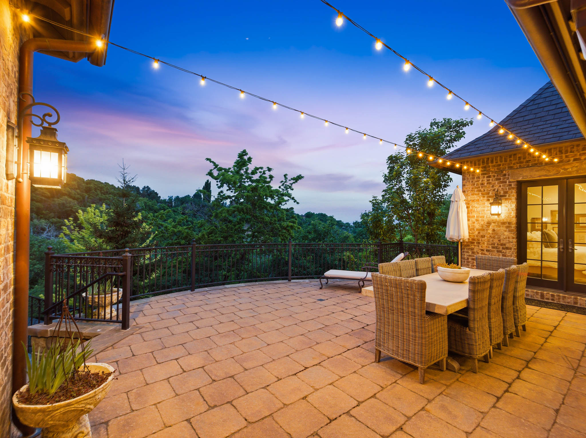 Expansive paver patio with string lighting and a durable wrought iron railing