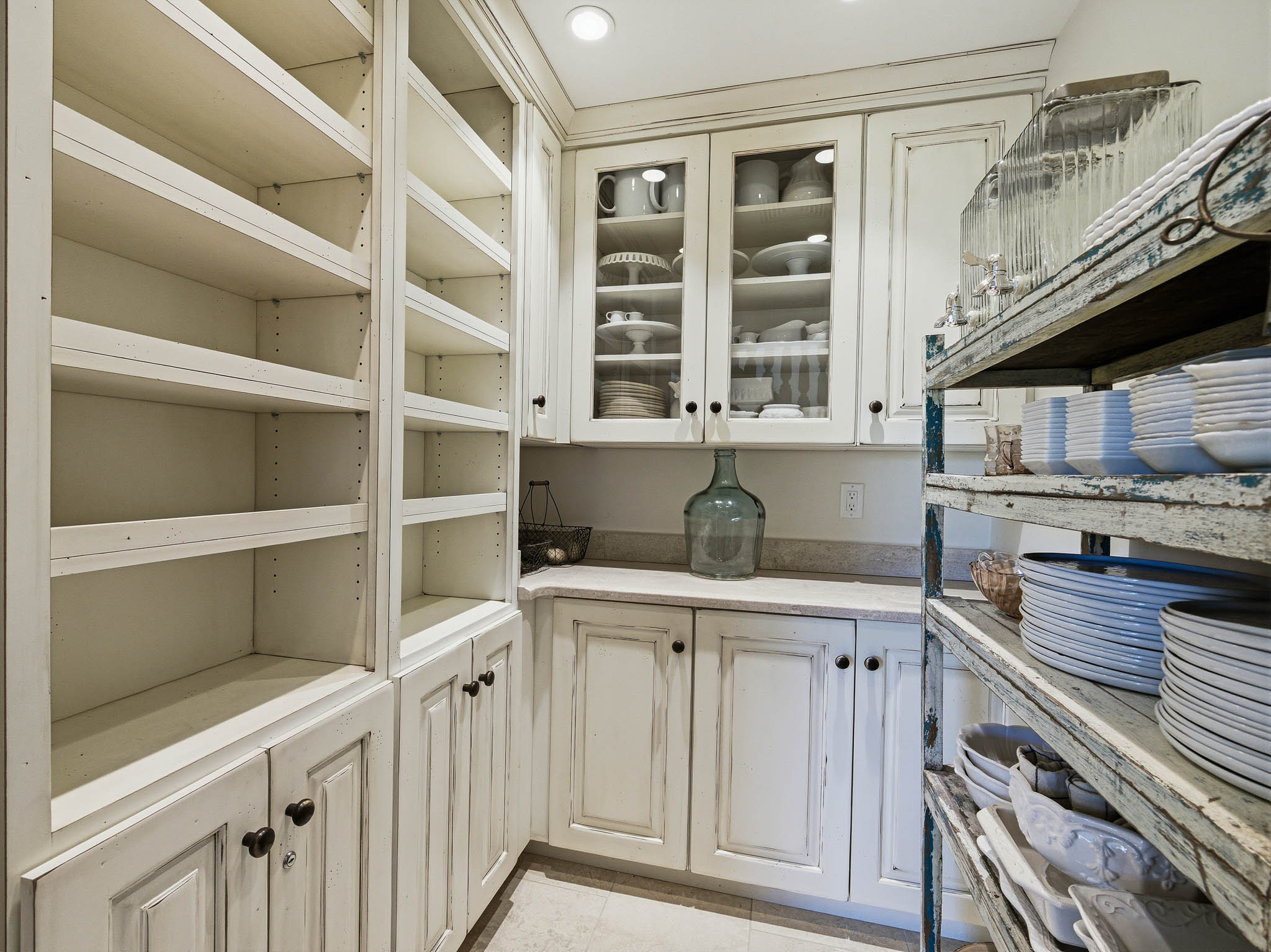 Integrated storage solutions featuring extensive built-in shelving, cabinet storage, glass-front upper cabinetry, and a light-toned countertop