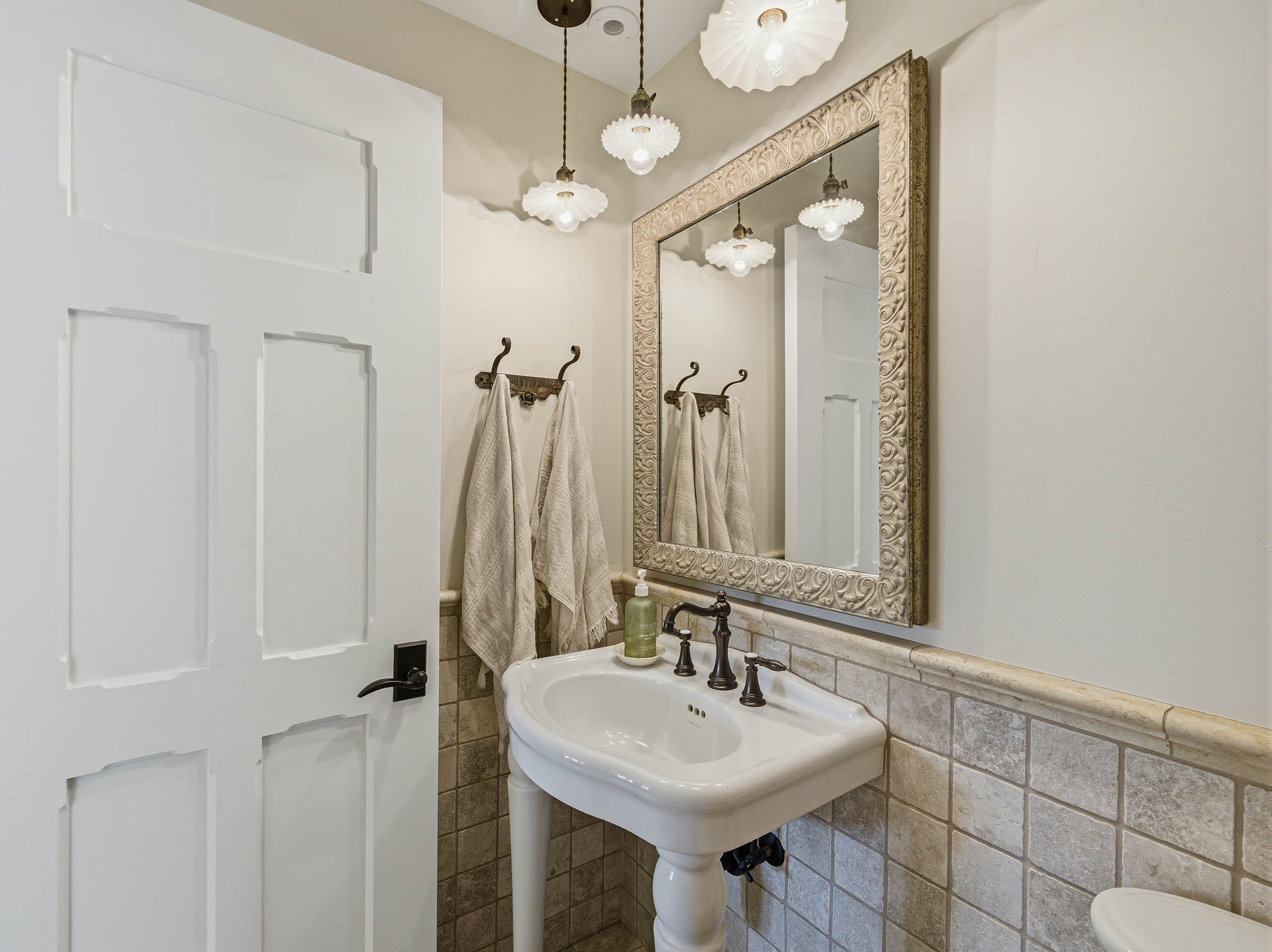 Pedestal sink with dark bronze faucet set, complemented by a framed mirror and two pendant light fixtures