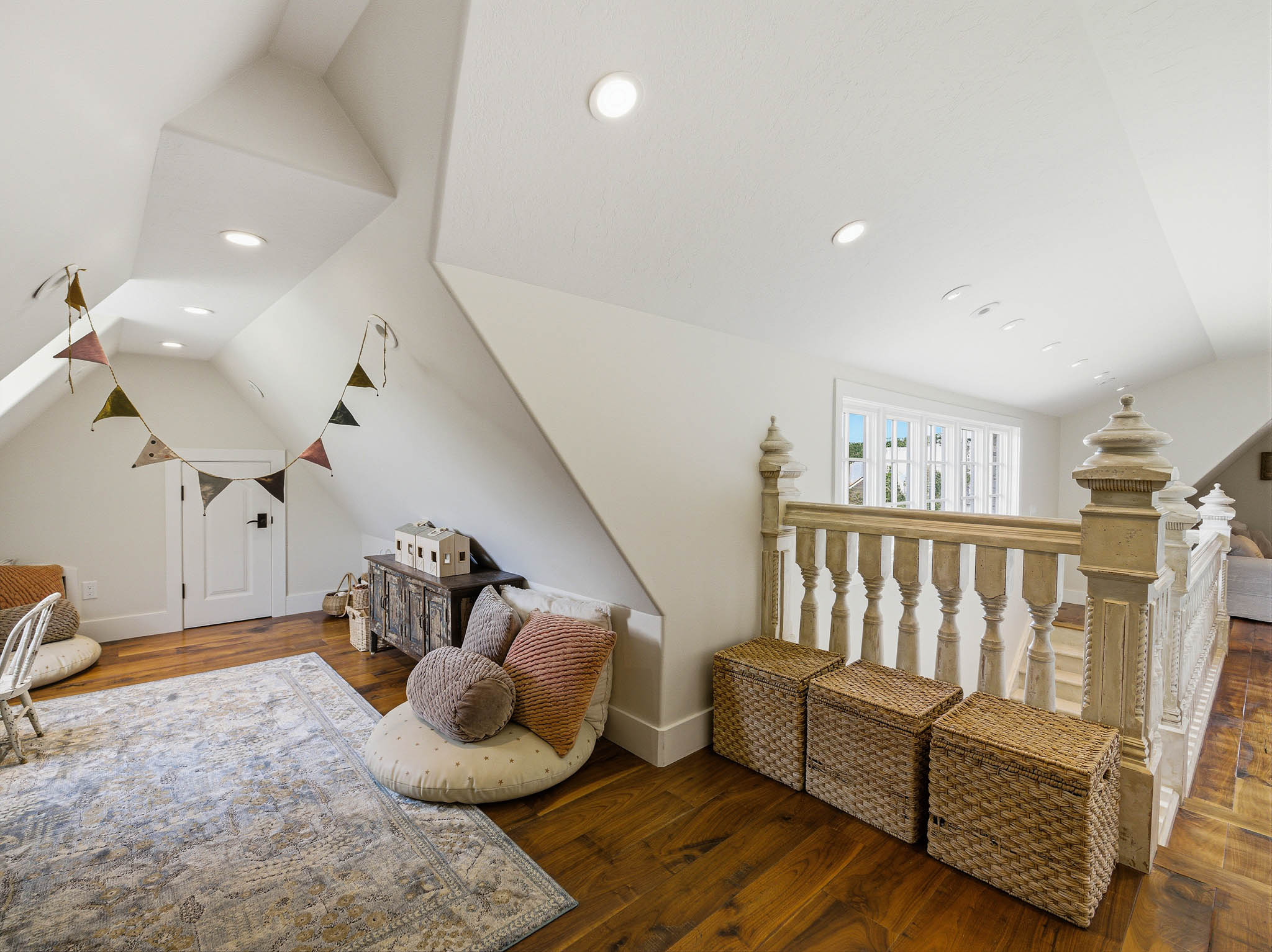 Upper level space featuring rich wood-finish flooring, a painted spindle railing, bright recessed lighting, a white paneled door, and a multi-pane window
