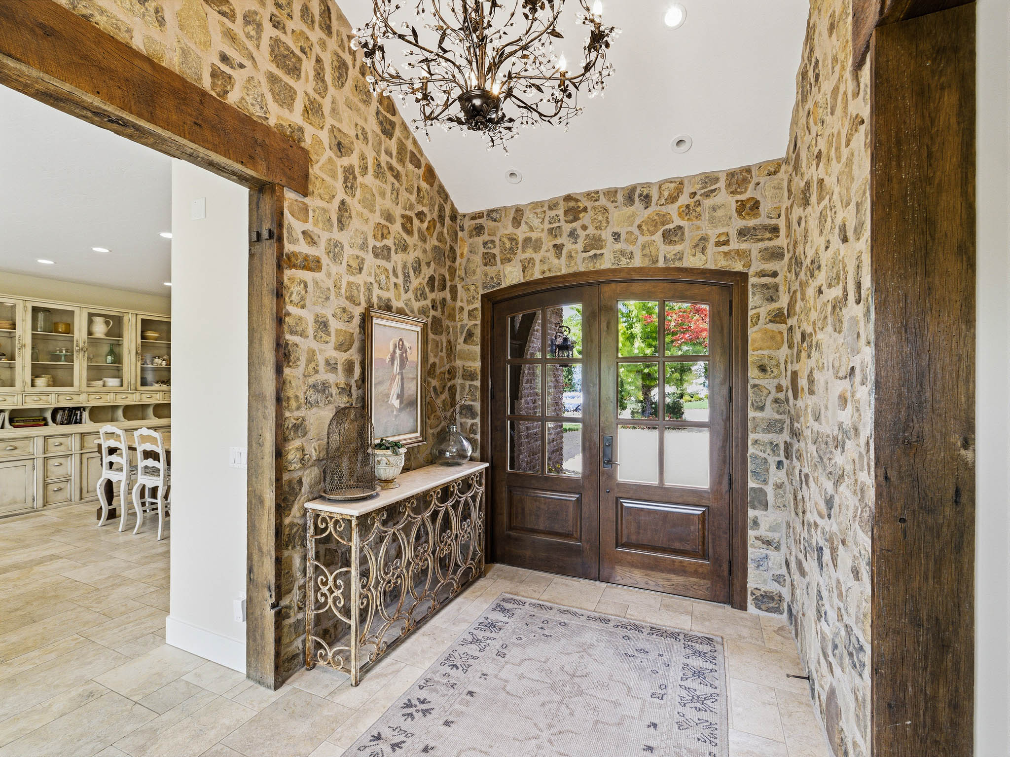 Grand entry featuring a vaulted ceiling with an ornate chandelier, stone accent walls, arched double-door entryway, and tile flooring