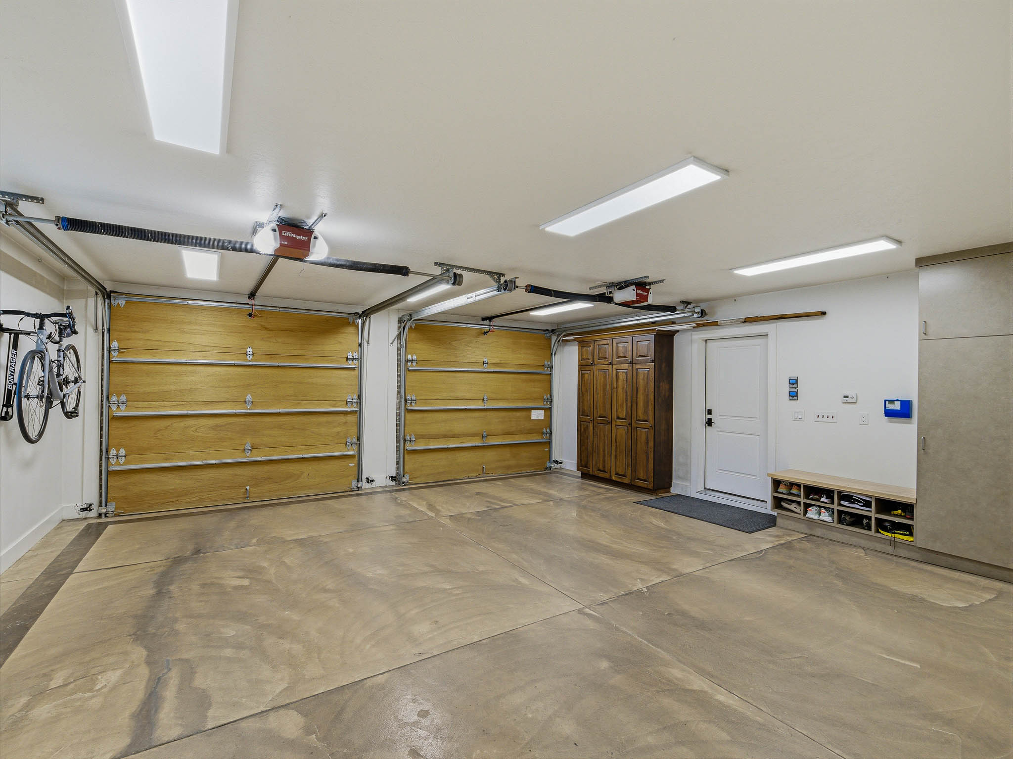 Spacious garage featuring a concrete floor, two wood-paneled garage doors with automatic openers, overhead fluorescent lighting, built-in wood cabinetry, and a white entry door