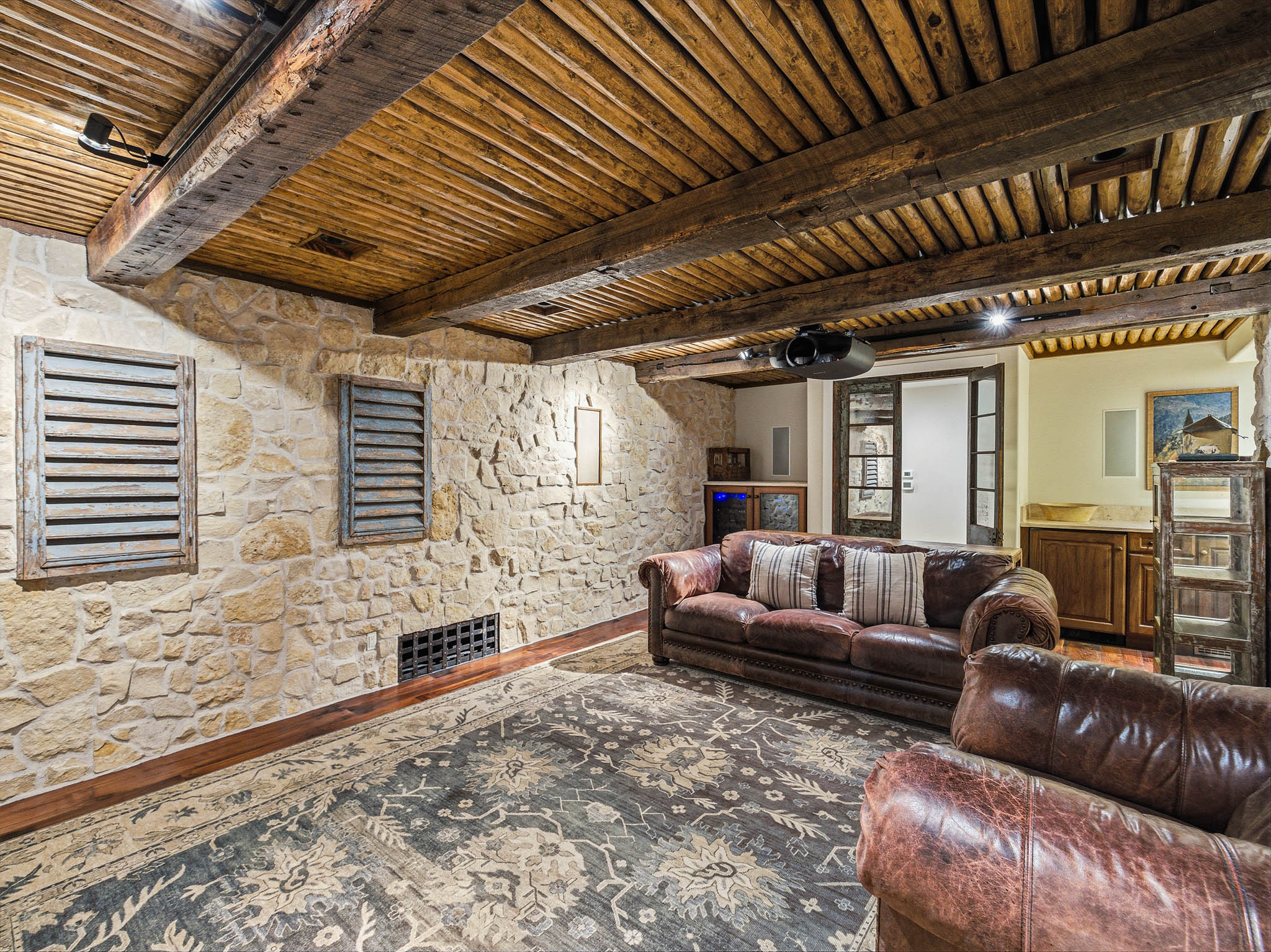 Exposed wood beam ceiling with natural wood planking, stone accent walls, dark wood-finish flooring, and built-in wet bar with stone countertop