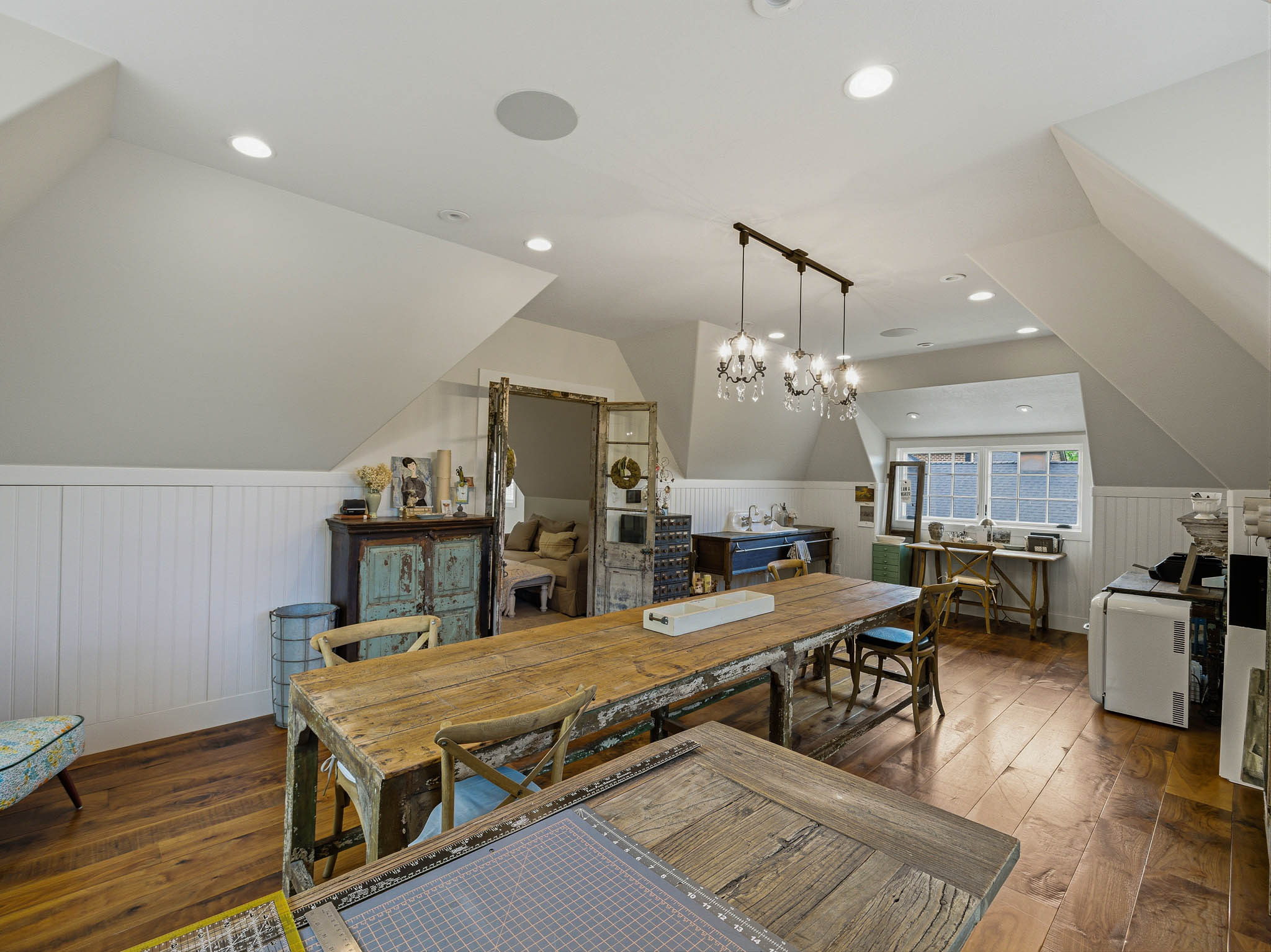 Spacious attic room featuring wood-finish flooring, white wainscoting, recessed lighting, and a multi-light chandelier