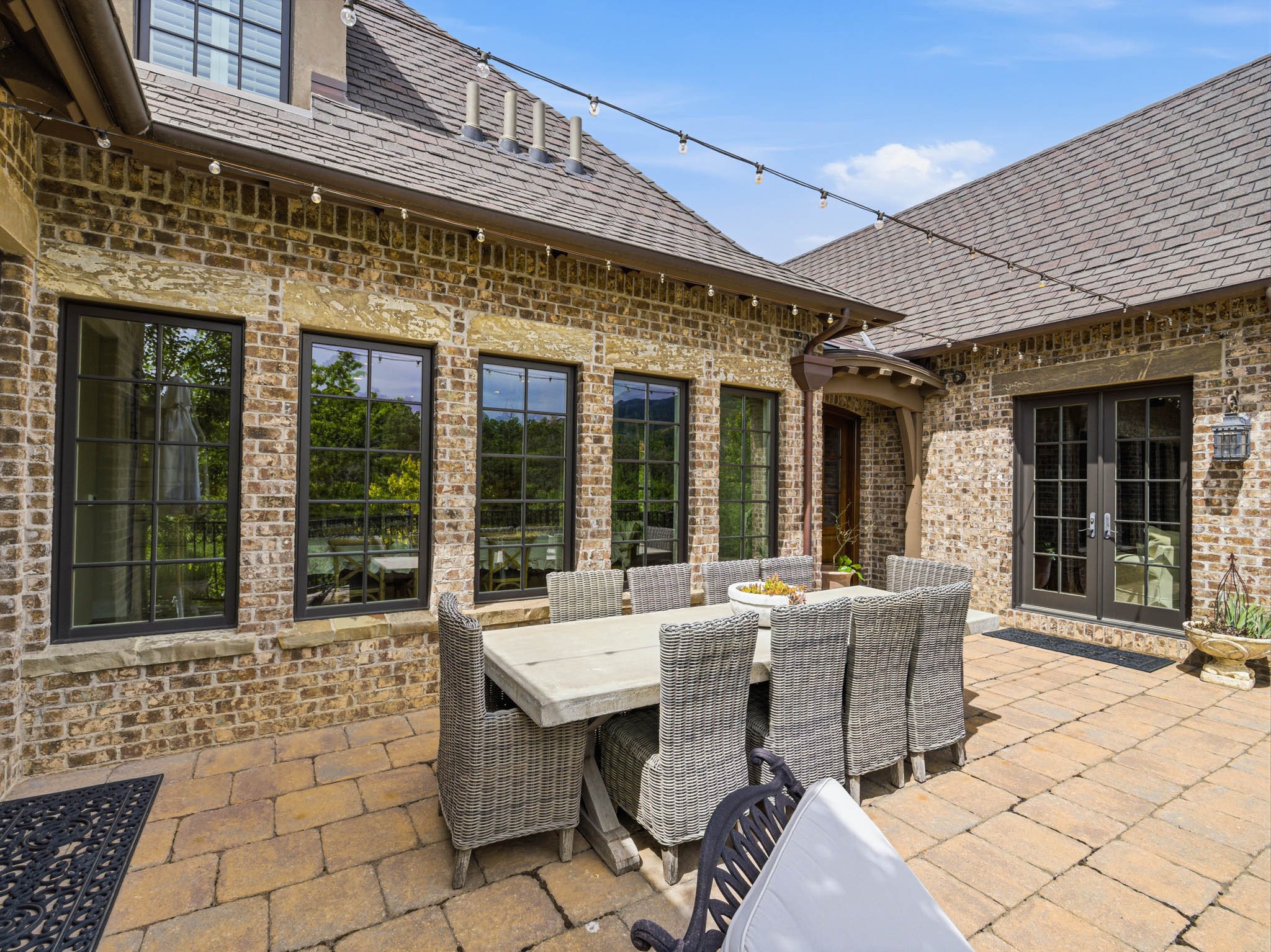 Expansive paver patio with a brick and stone facade, multiple large windows, and double French doors