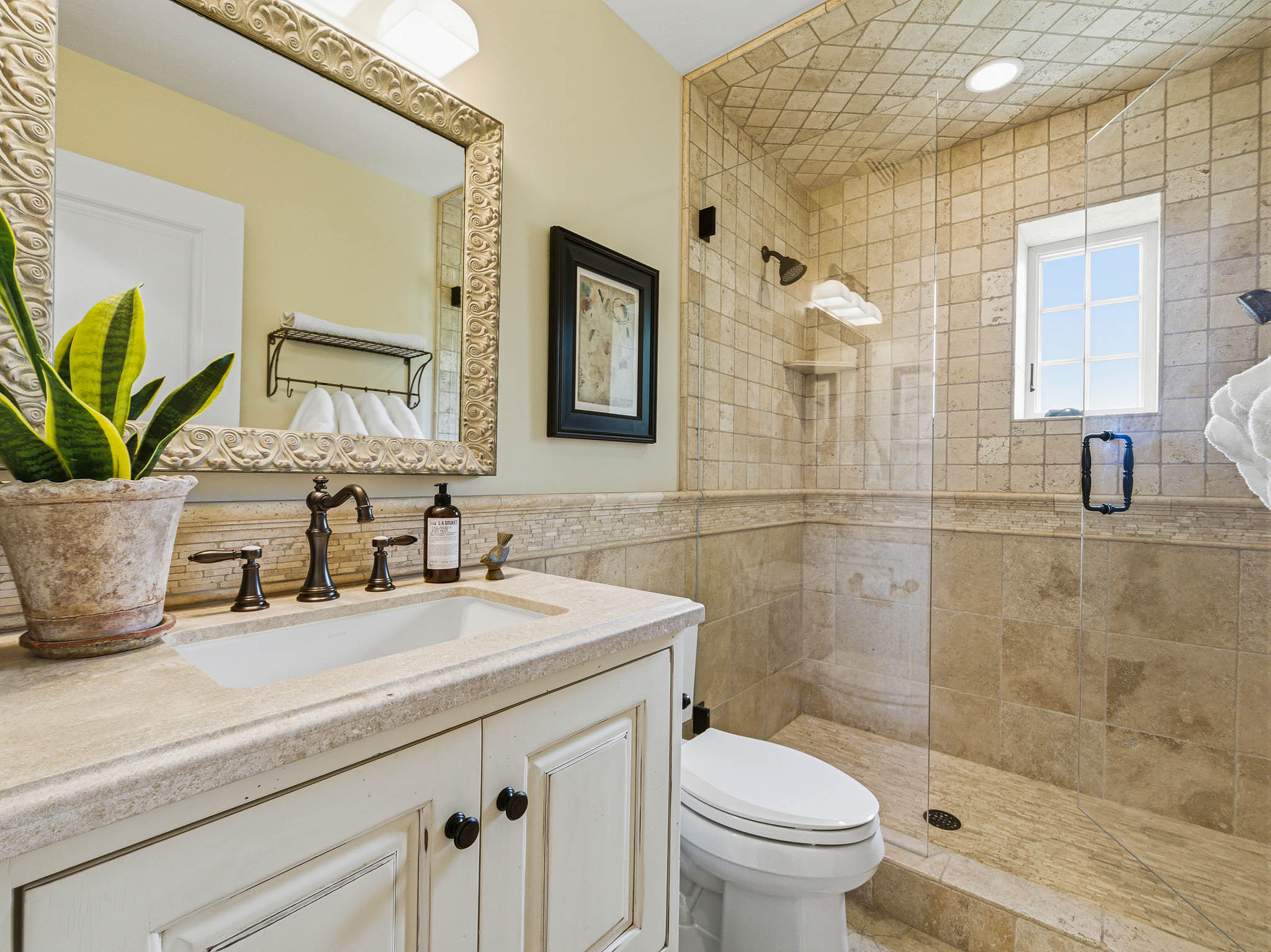 Bathroom featuring a glass-enclosed shower with tile surround, a built-in window, a vanity with a rectangular sink, and an ornate framed mirror