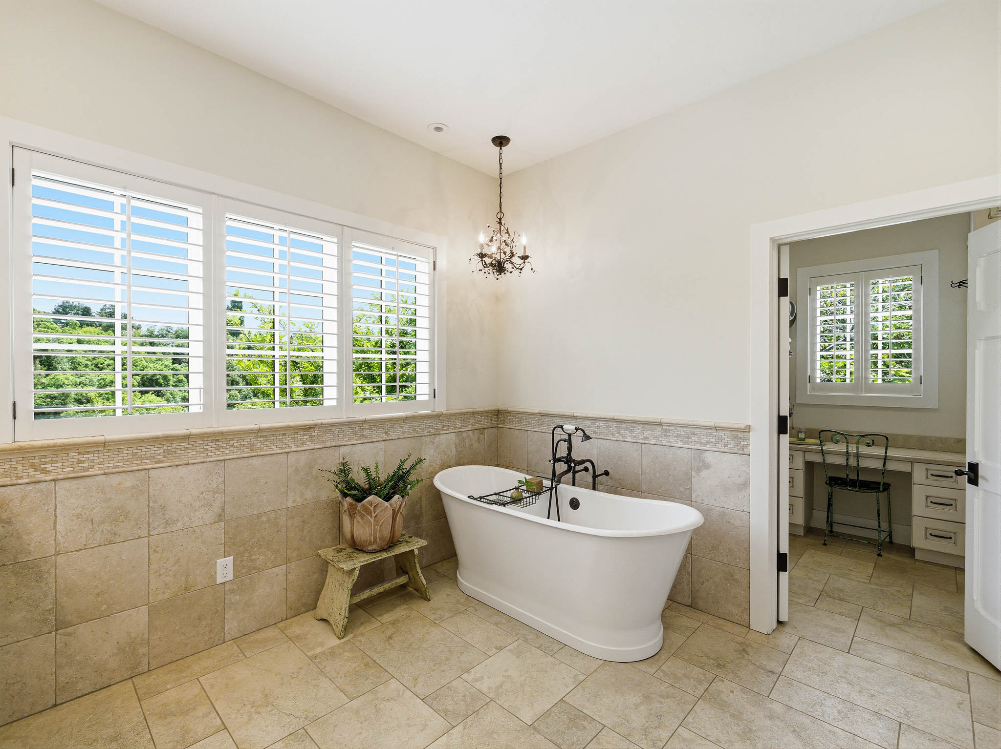 Freestanding soaking tub with a floor-mounted faucet, complemented by large format floor tiles and coordinating wall tile wainscoting