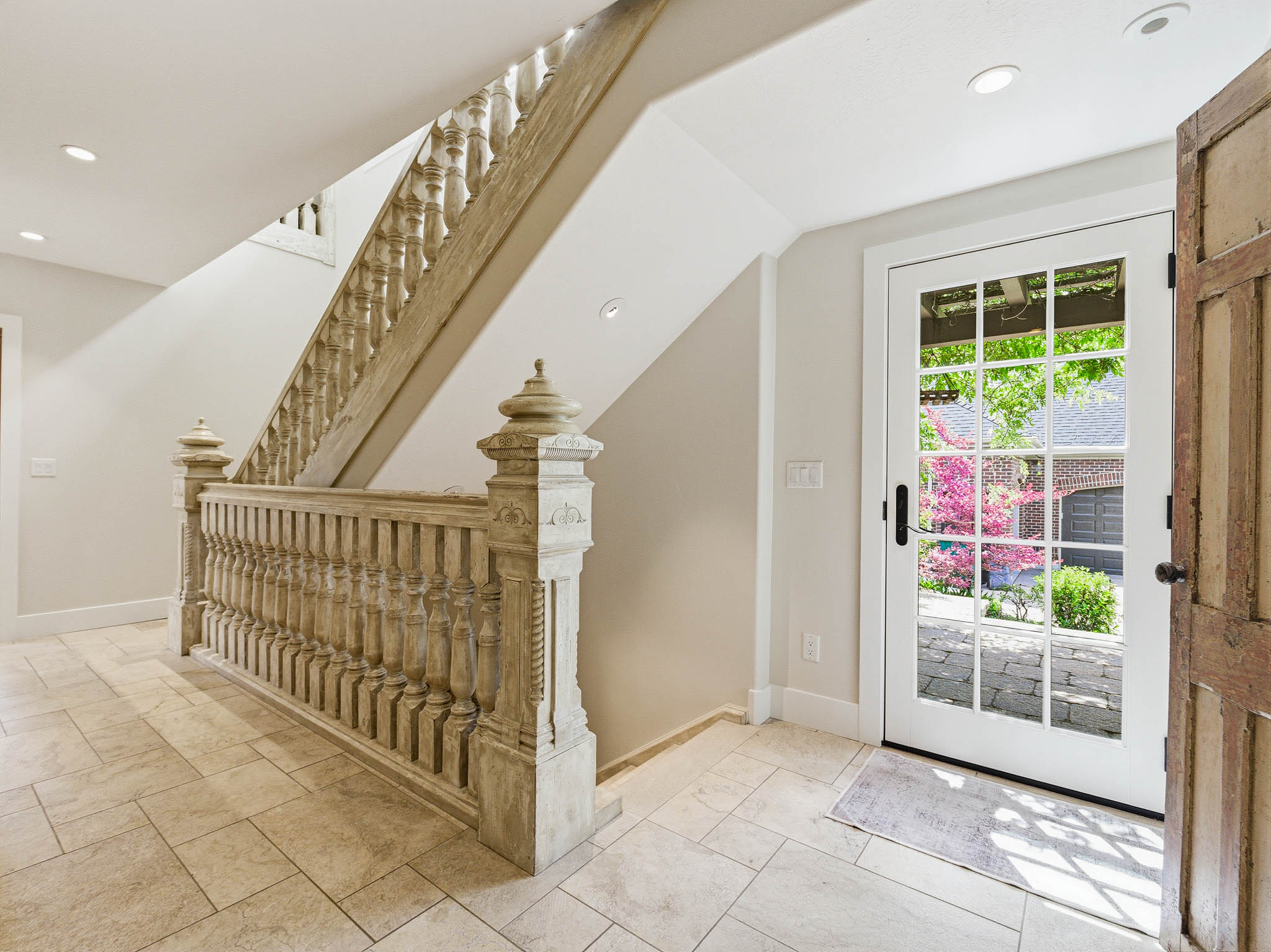Entryway featuring an ornate wood staircase, light-toned rectangular floor tiling, a white paneled door with glass inserts, recessed ceiling lighting, and neutral wall paint