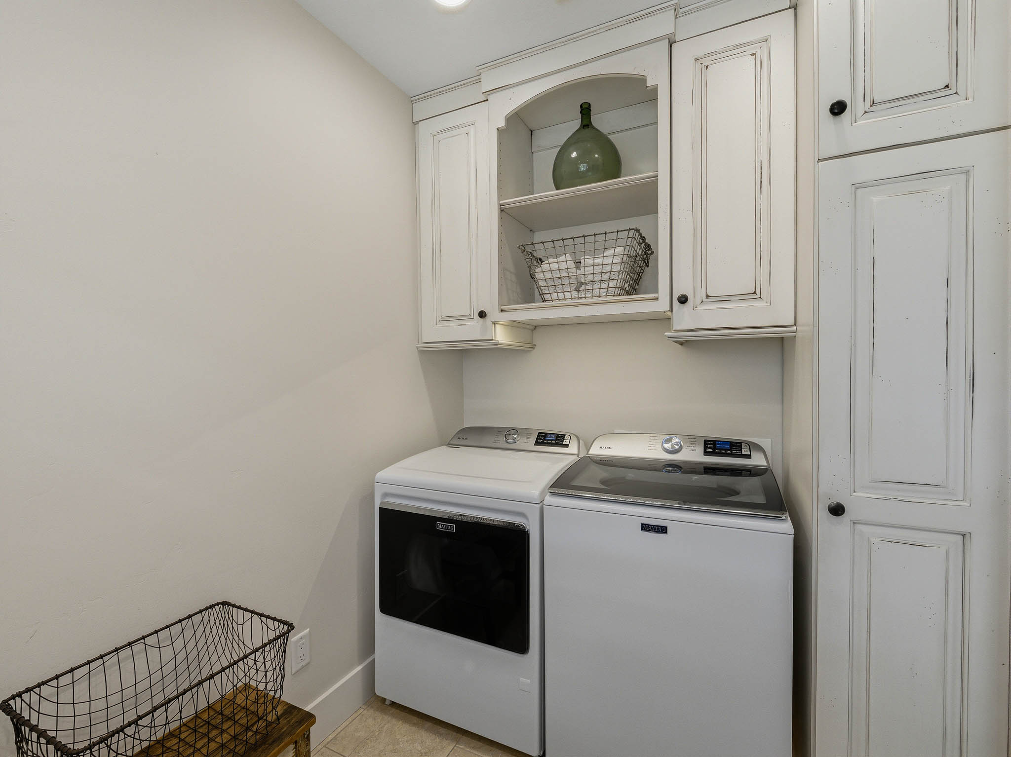 Laundry area featuring distressed white cabinetry with black hardware, built-in shelving, and a neutral wall color