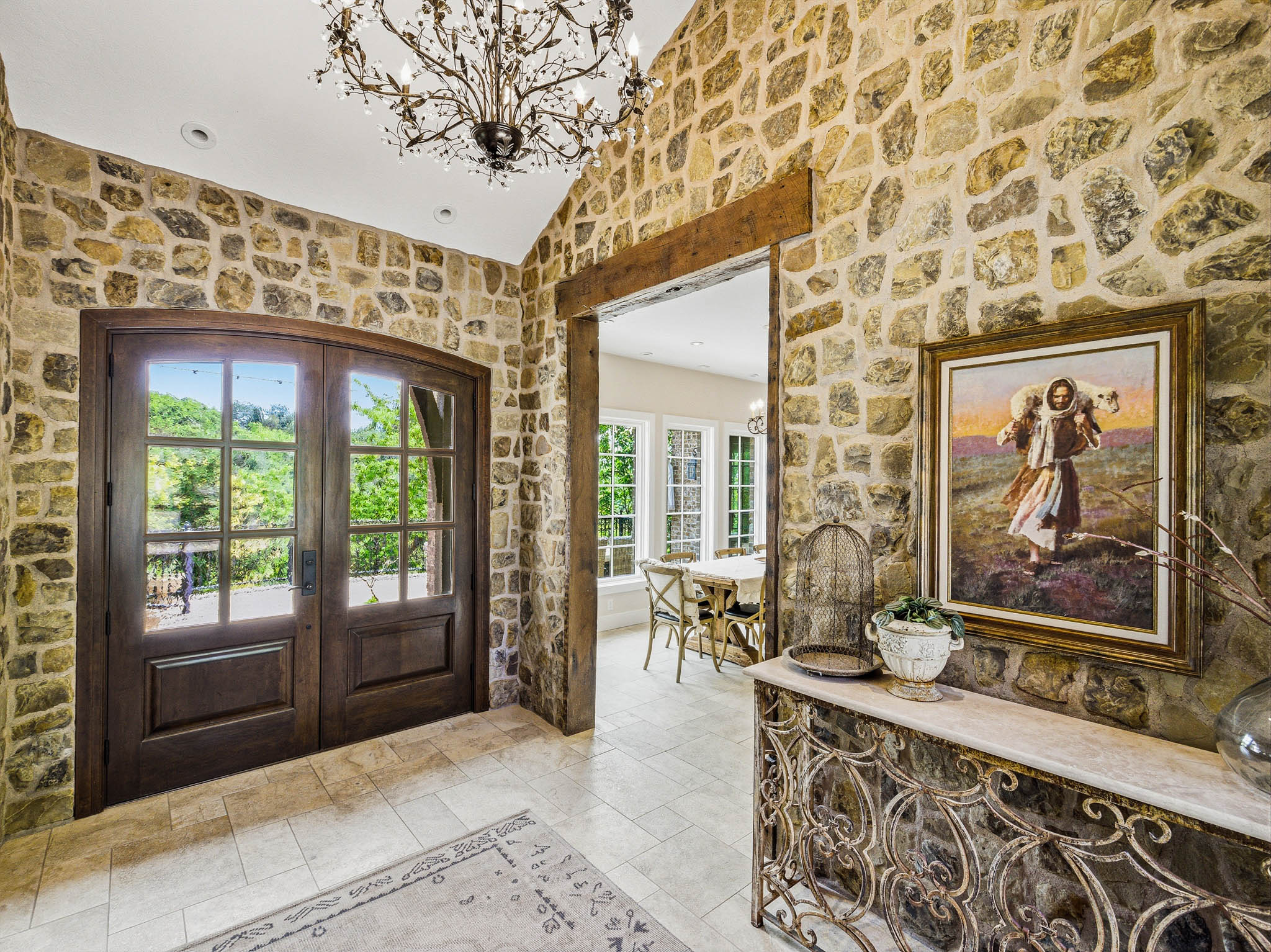 Entryway featuring stone-clad walls, vaulted ceiling with a decorative chandelier, and double arched wood-frame doors with glass panels