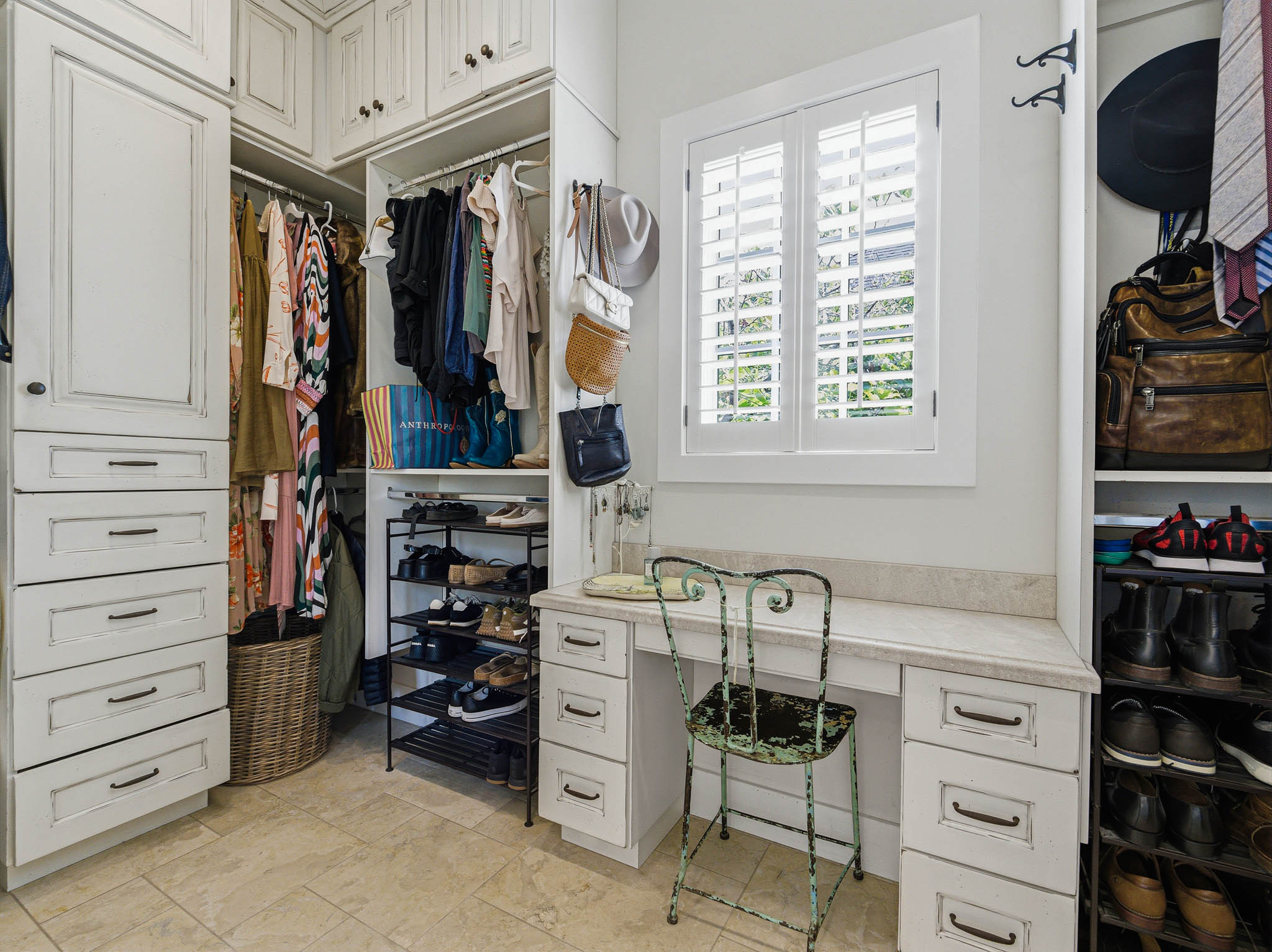 Custom-designed closet system featuring built-in cabinetry, upper storage, open shelving, and a dedicated vanity with a stone countertop