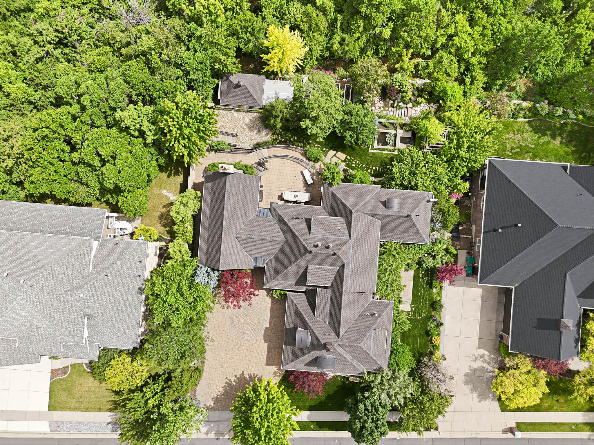 Sprawling residential property featuring extensive mature landscaping, multiple paved patios, and a gravel driveway