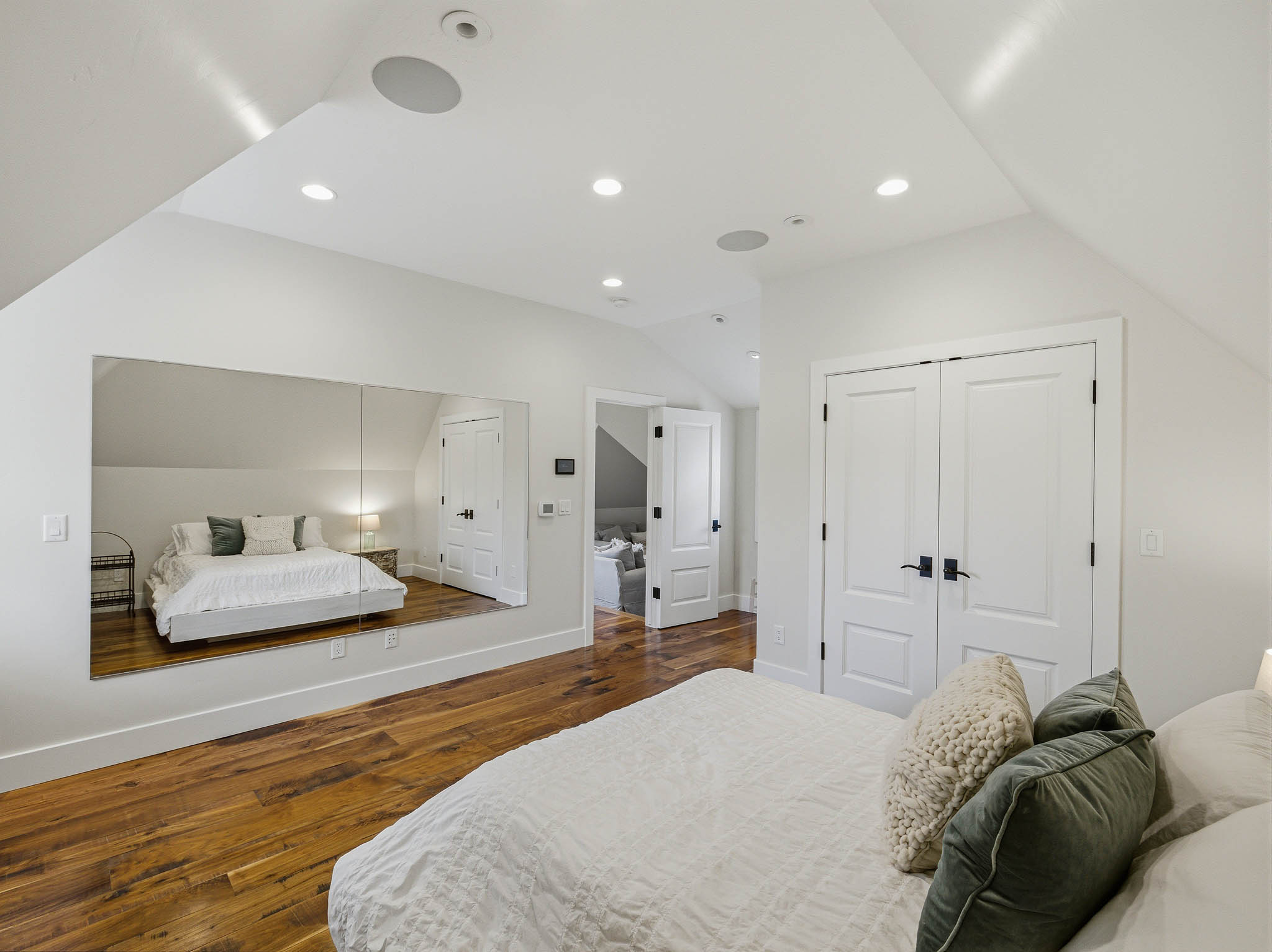 Attic bedroom featuring rich wood-finish flooring, recessed lighting, and a mirrored accent wall