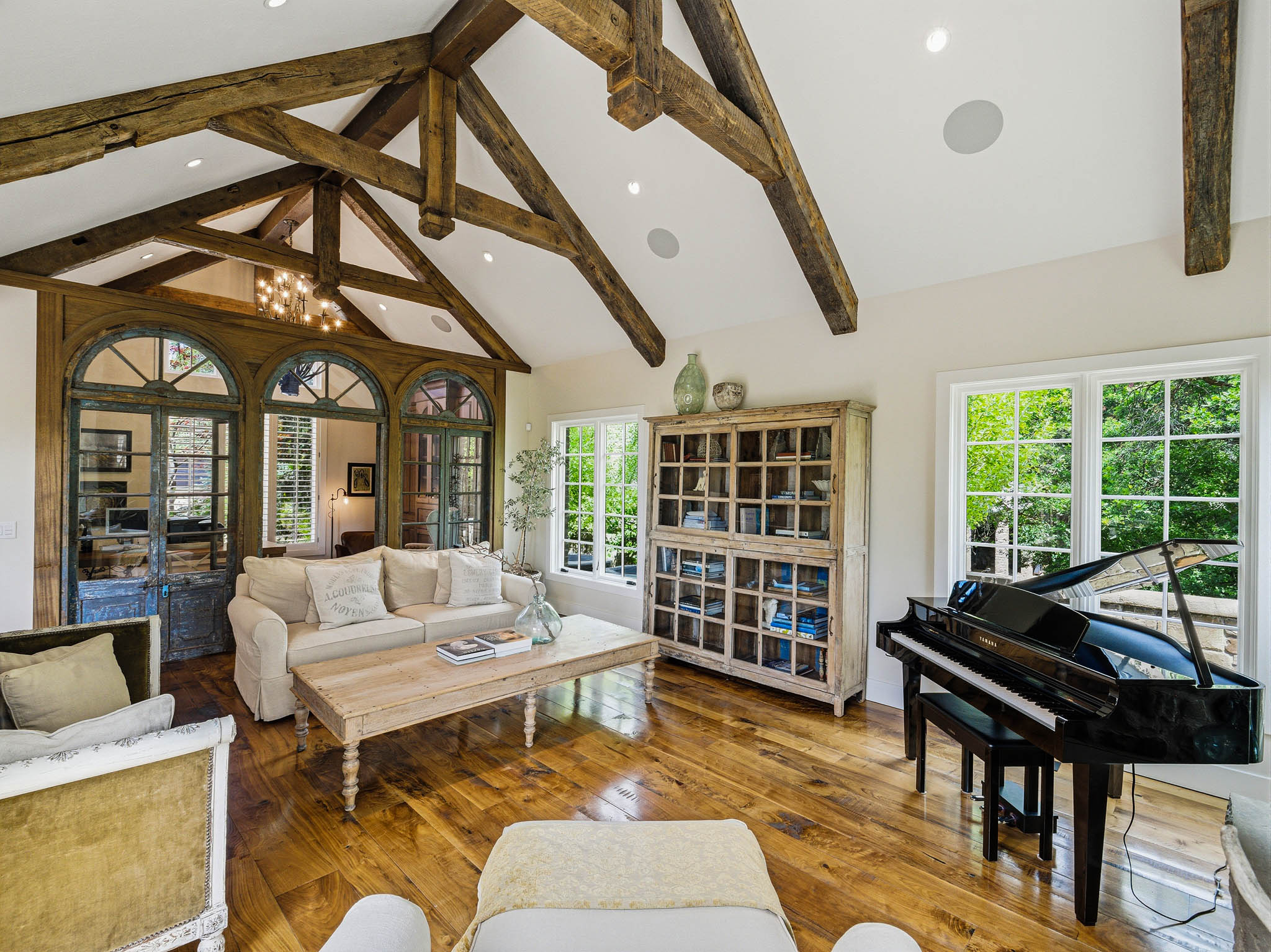 Vaulted ceiling with exposed wood beams, wood-finish flooring, and multiple large windows