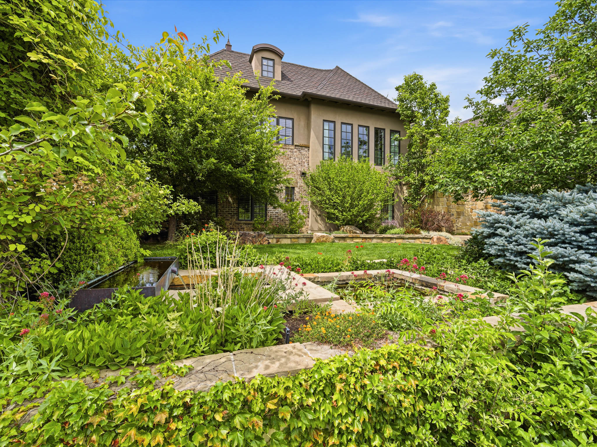Multi-level terraced garden featuring extensive plantings, a water feature, and stone retaining walls
