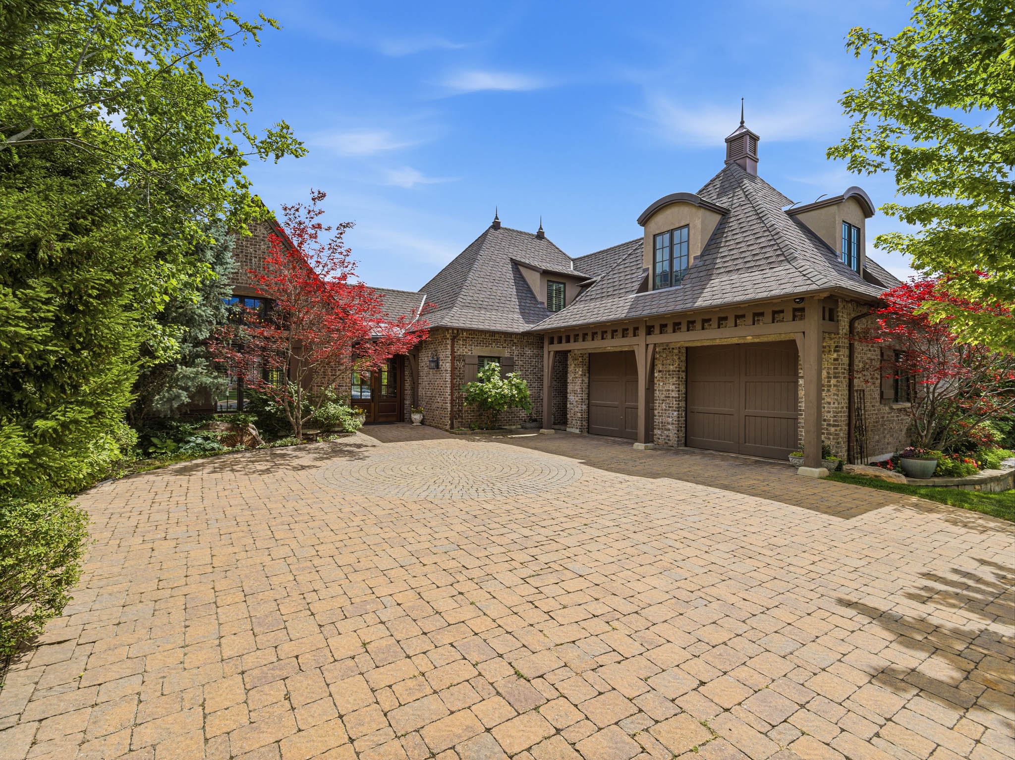 Stone and stucco exterior featuring a multi-car garage with wood-finish doors, a turret, and a paver driveway
