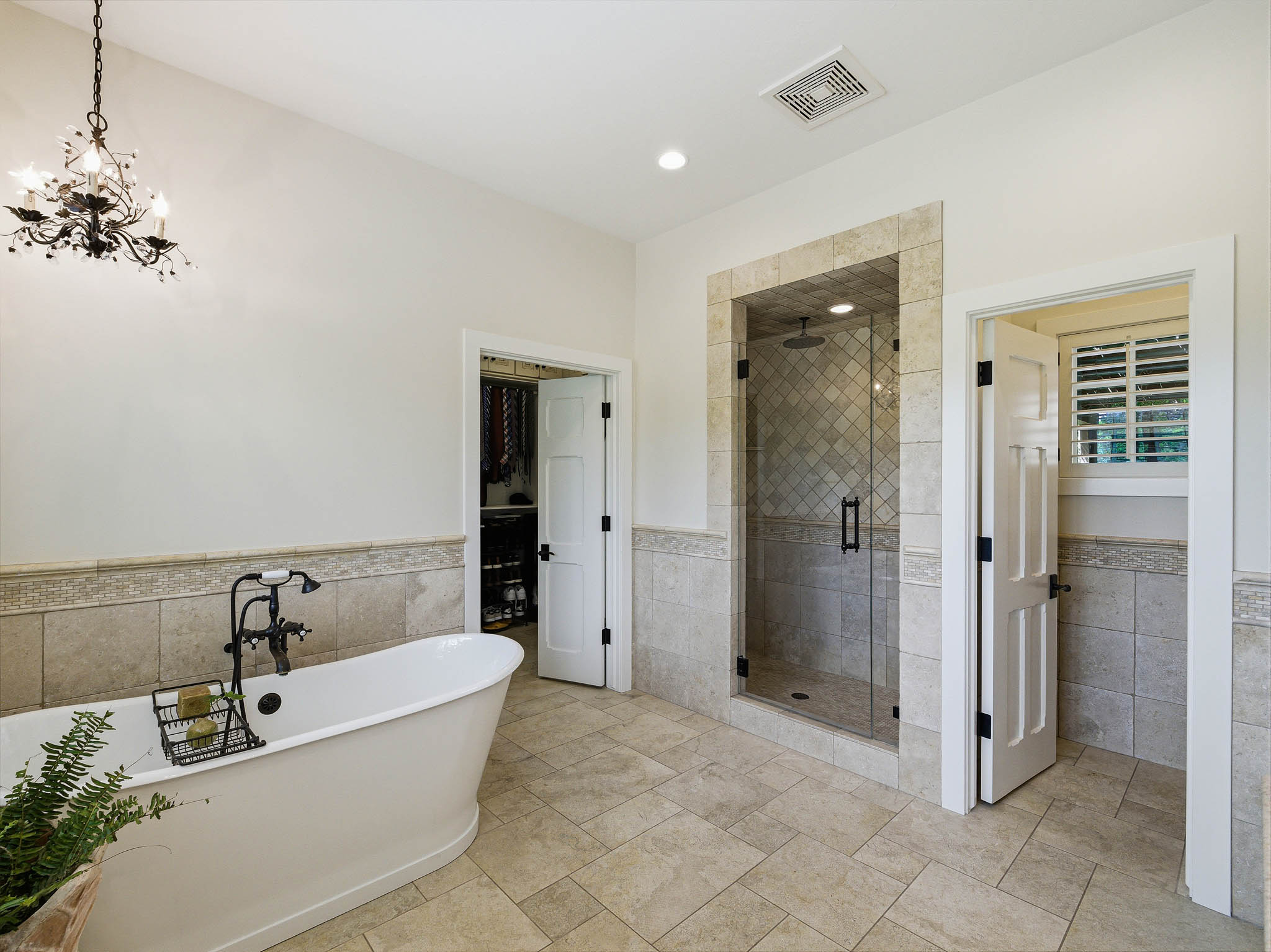 Spacious bathroom featuring a freestanding soaking tub with a floor-mounted fixture, a glass-enclosed shower with tile surround, and neutral-toned tile flooring