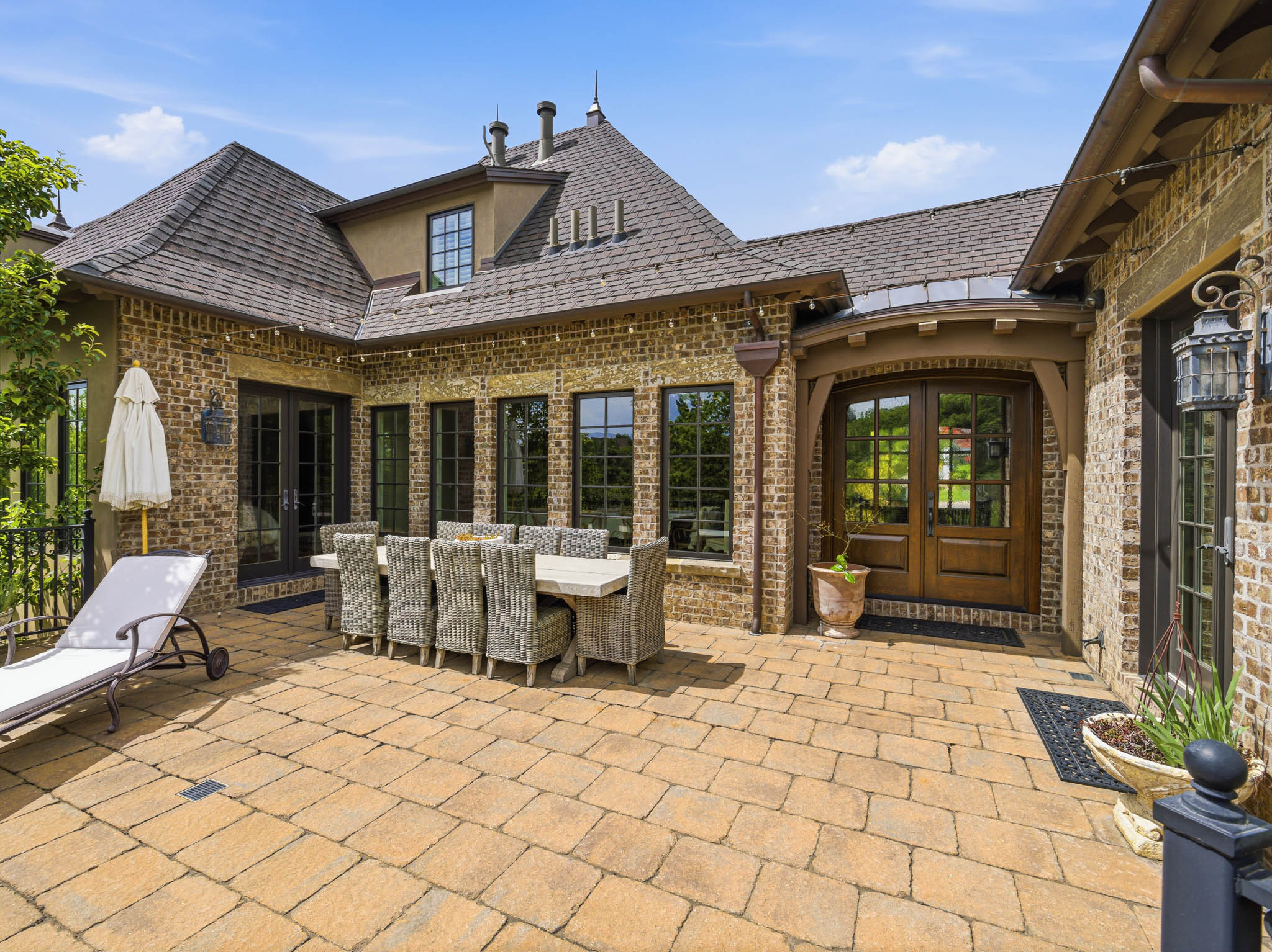 Expansive paver patio with a brick exterior, multiple windows, and a prominent double entry door with glass panels
