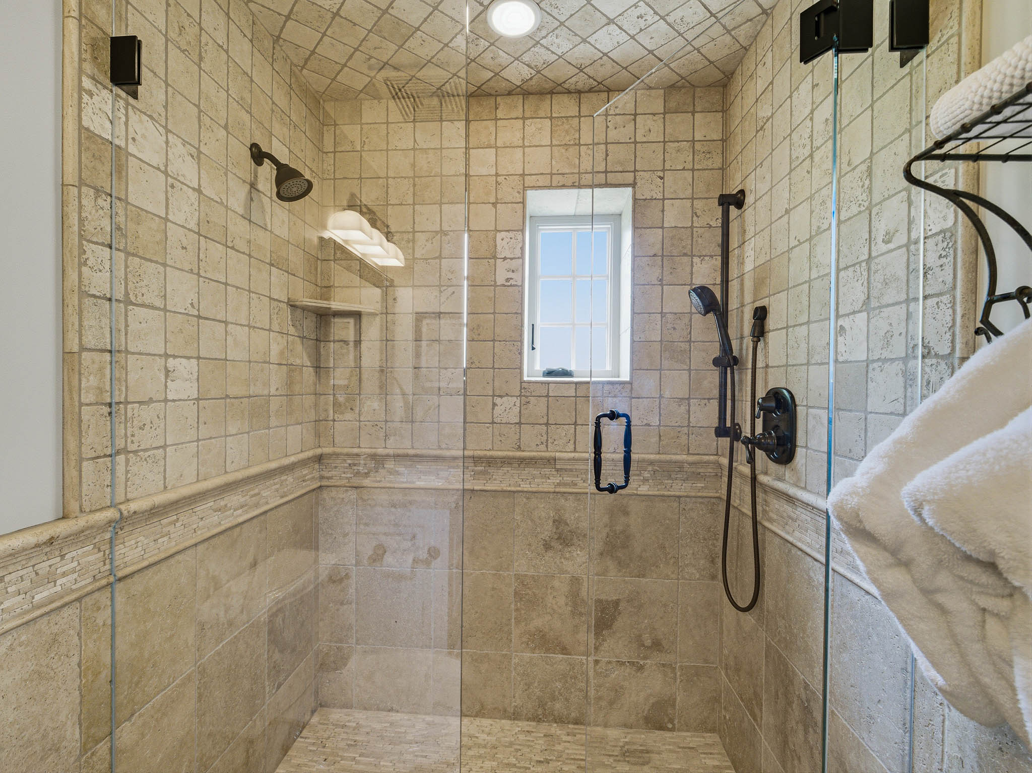 Tiled shower enclosure featuring a clear glass door, oil-rubbed bronze fixtures, a recessed window, and a built-in shower niche