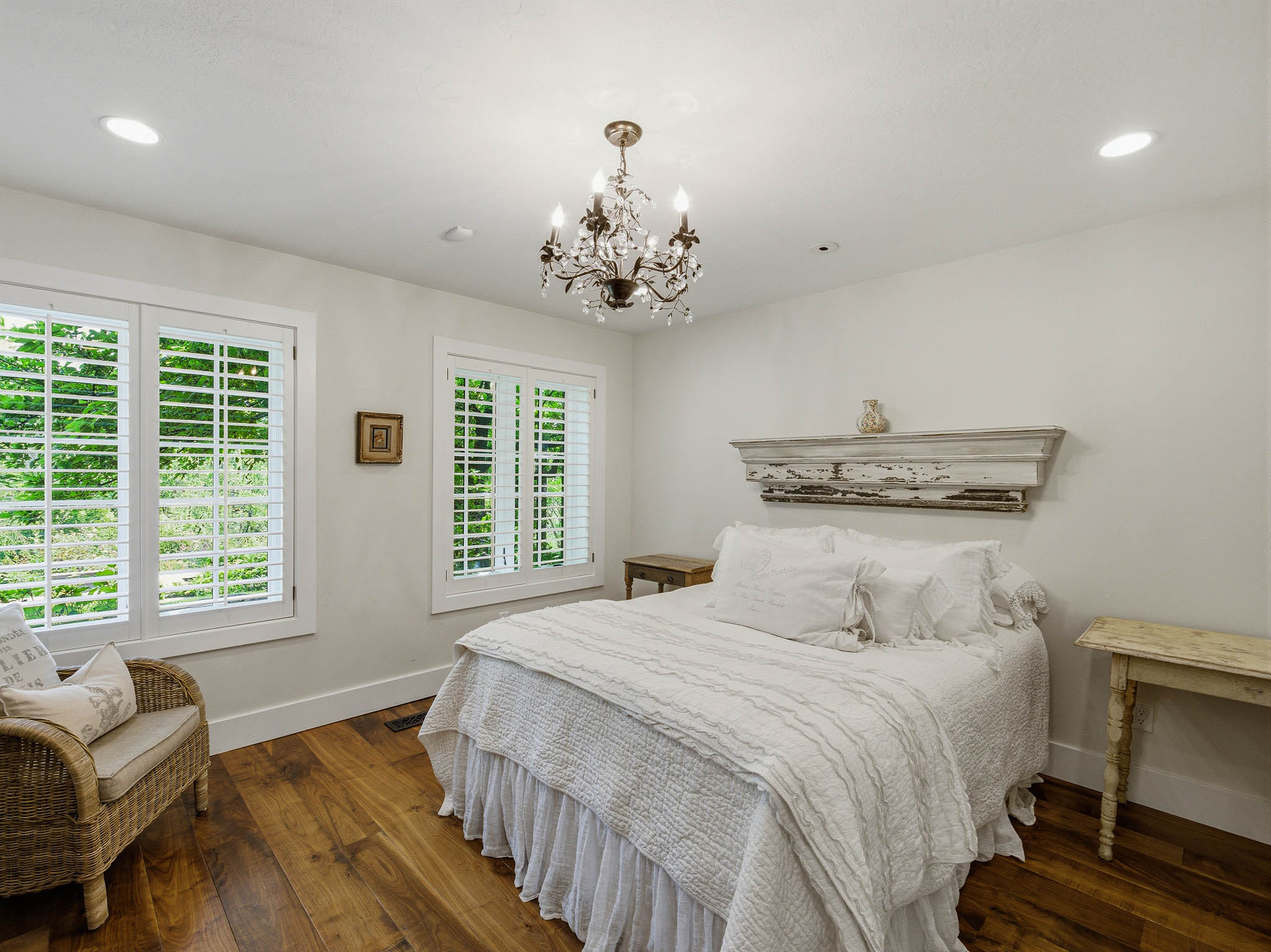 Room featuring wood-finish flooring, two large windows with white louvered shutters, a crystal chandelier, and recessed ceiling lighting