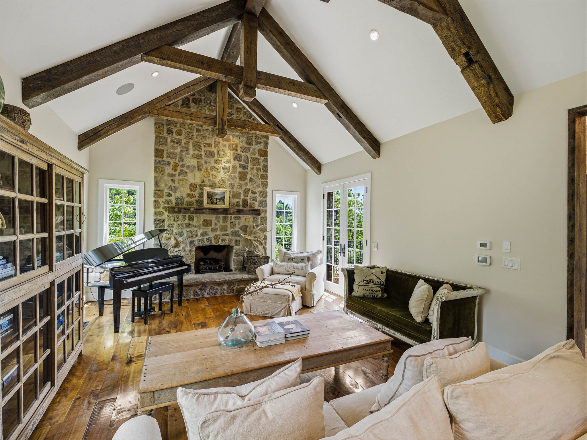 Living space featuring a vaulted ceiling with exposed wood beams, a stone-clad fireplace, wood-finish flooring, and French doors