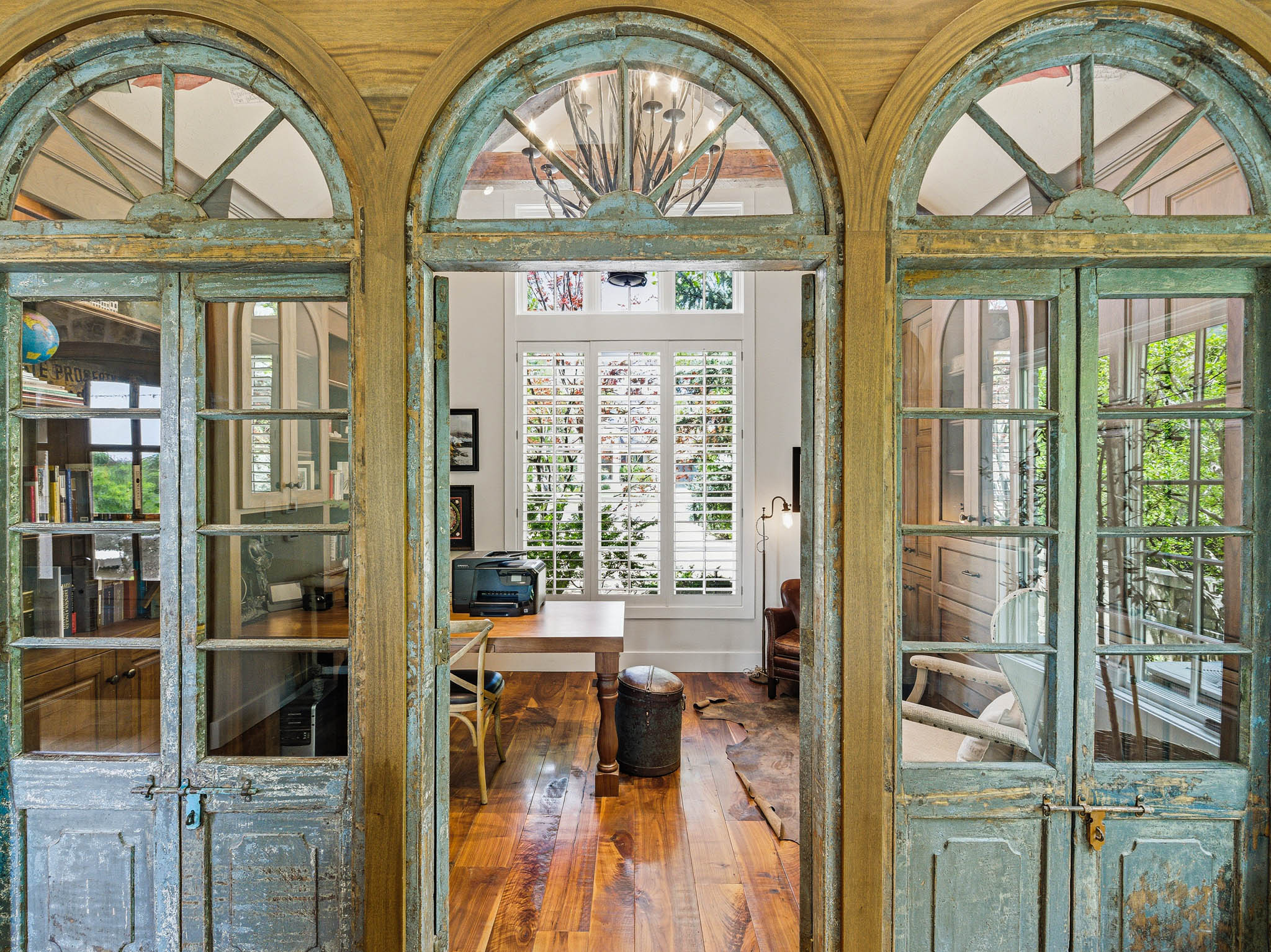 Arched entryways with distressed wood-finish doors open to a room featuring wide plank wood-finish flooring, white plantation shutters, a vaulted ceiling, and built-in cabinetry