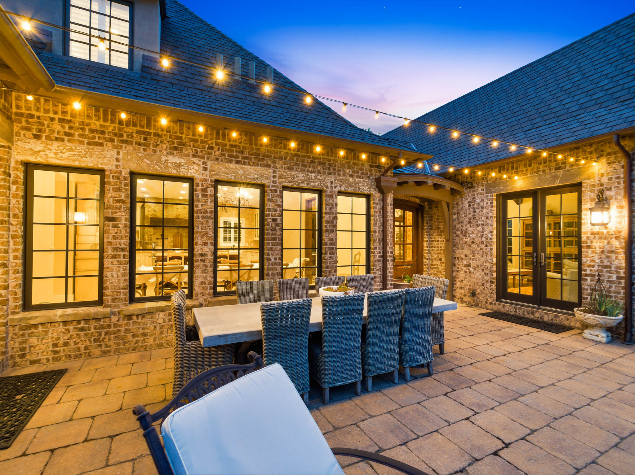 Spacious paver patio featuring string lighting, multiple black-framed windows, and double French doors with transom windows