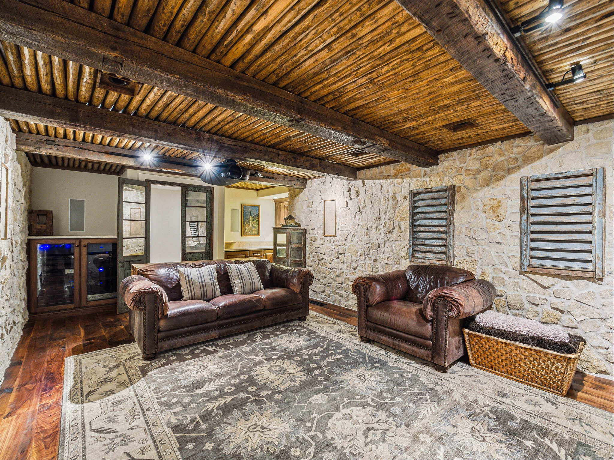 Stone-clad interior room featuring a wood-beam ceiling, wood-finish flooring, and built-in media cabinetry