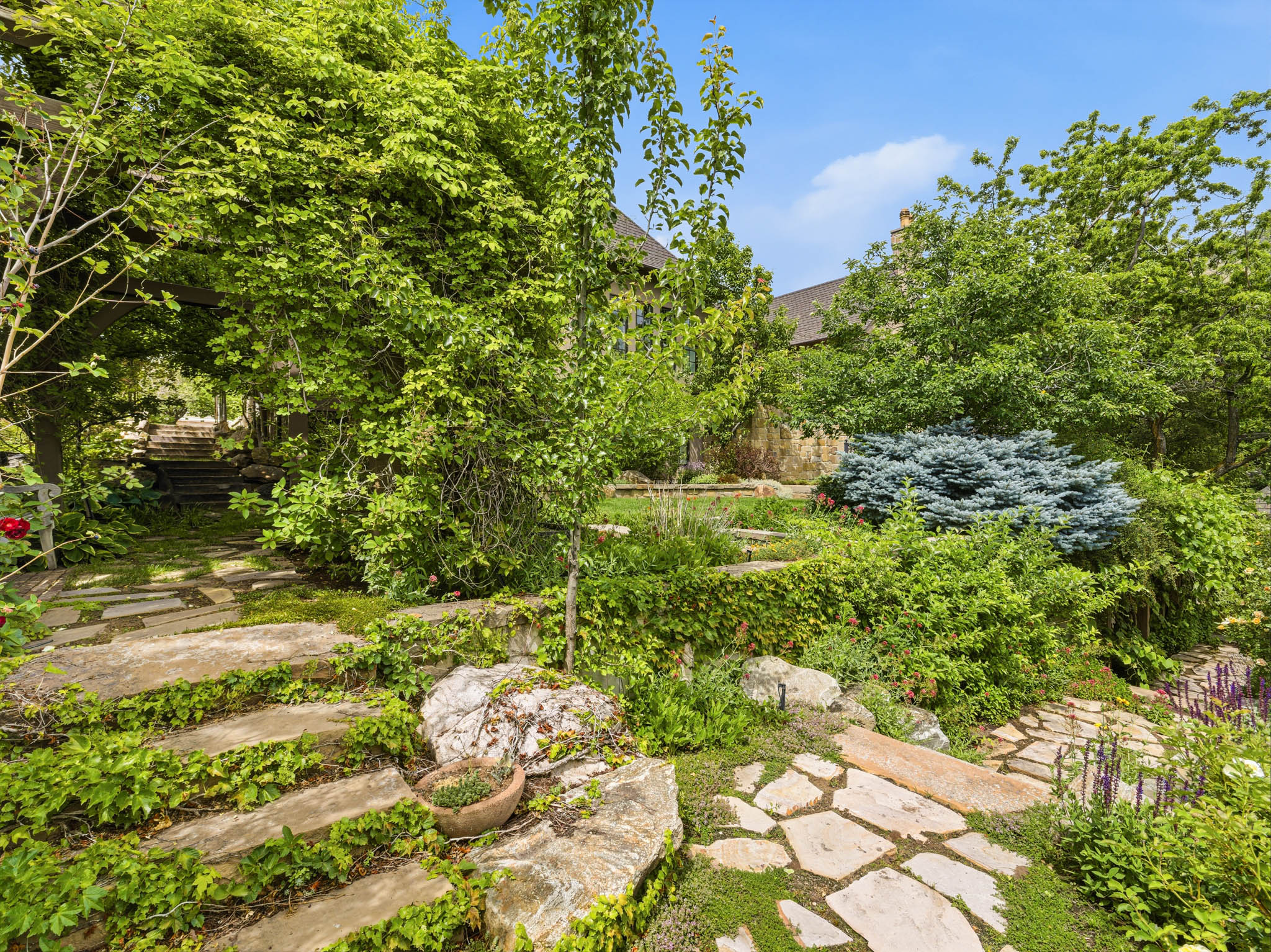 Extensive landscaping with flagstone pathways and steps, mature trees and shrubs, stone retaining walls, and planted garden beds