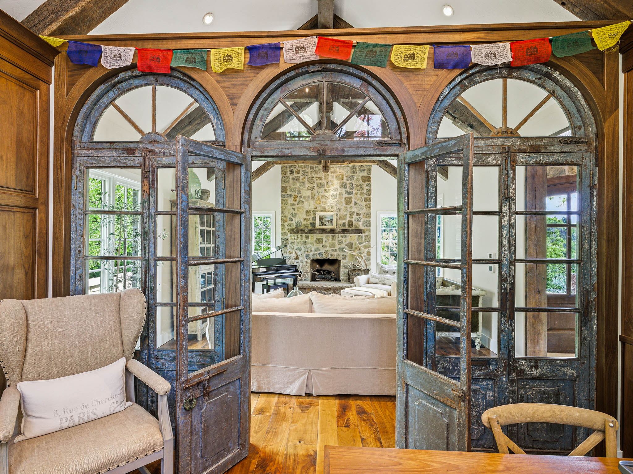 Distressed wood-frame French doors with arched transoms open to a living space featuring a stone fireplace