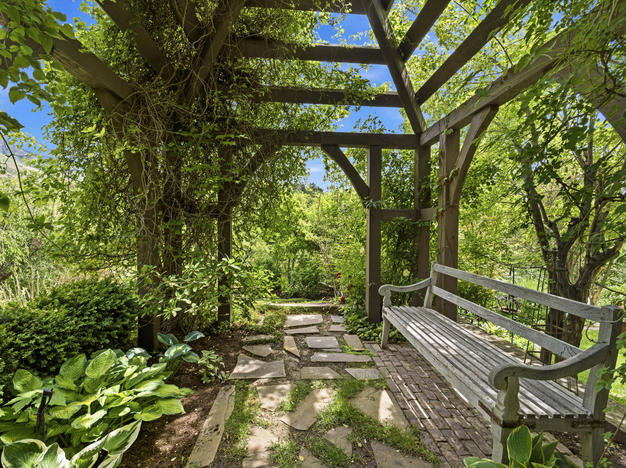 Wood pergola featuring climbing greenery, a stone slab pathway, and brick paver flooring
