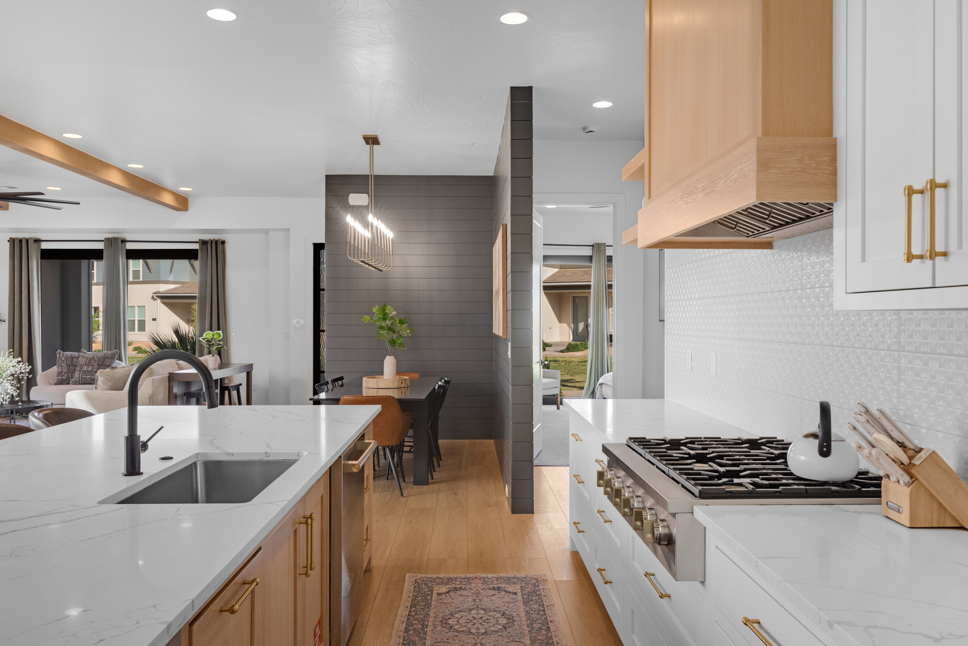 Gourmet kitchen with white countertops, a large island featuring an undermount sink and matte black faucet, a built-in range, a light wood-finish range hood, and white cabinetry with brass hardware