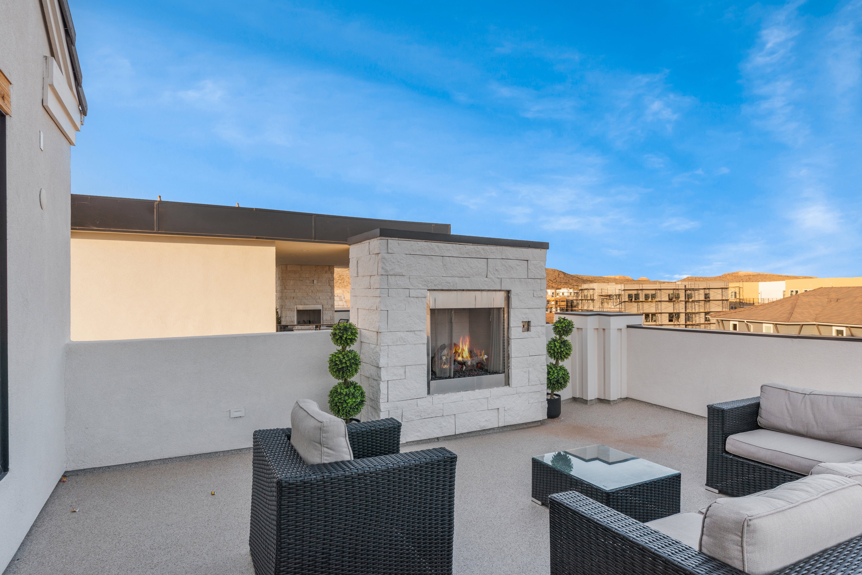 Rooftop patio featuring a stone-clad fireplace with a dark metal frame, a flat-top roofline, white stucco walls, and a textured gray flooring surface