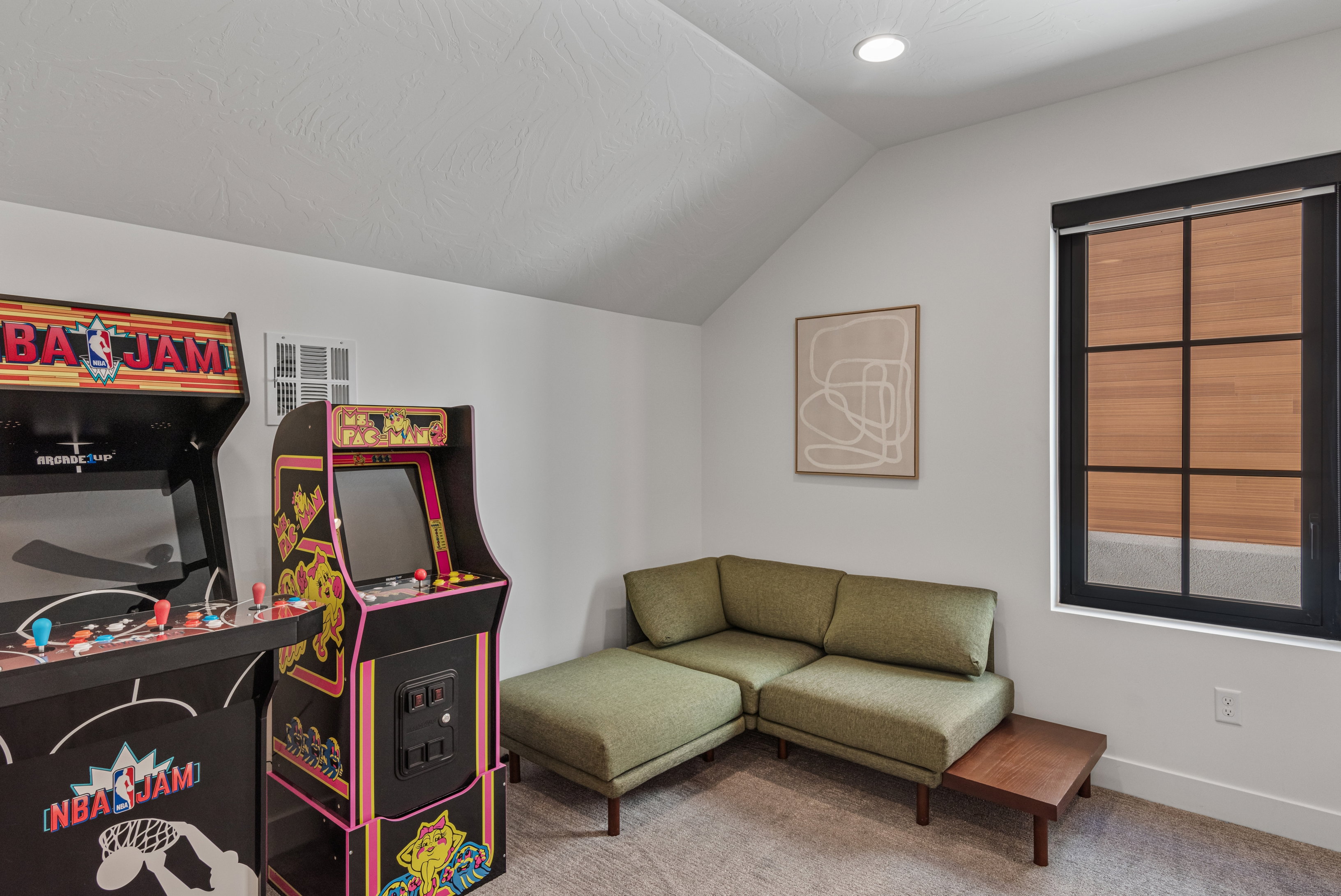 Attic space featuring a sloped ceiling, recessed lighting, and a black-framed window with integrated blinds