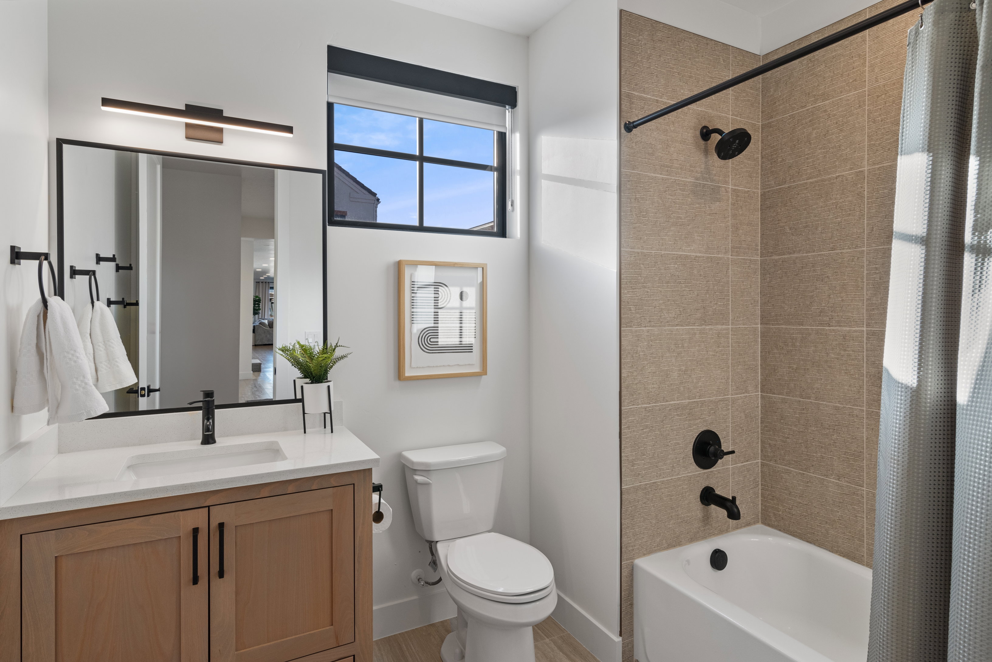 Contemporary bathroom featuring a light wood-finish vanity with white countertop, black-framed mirror, and matte black fixtures