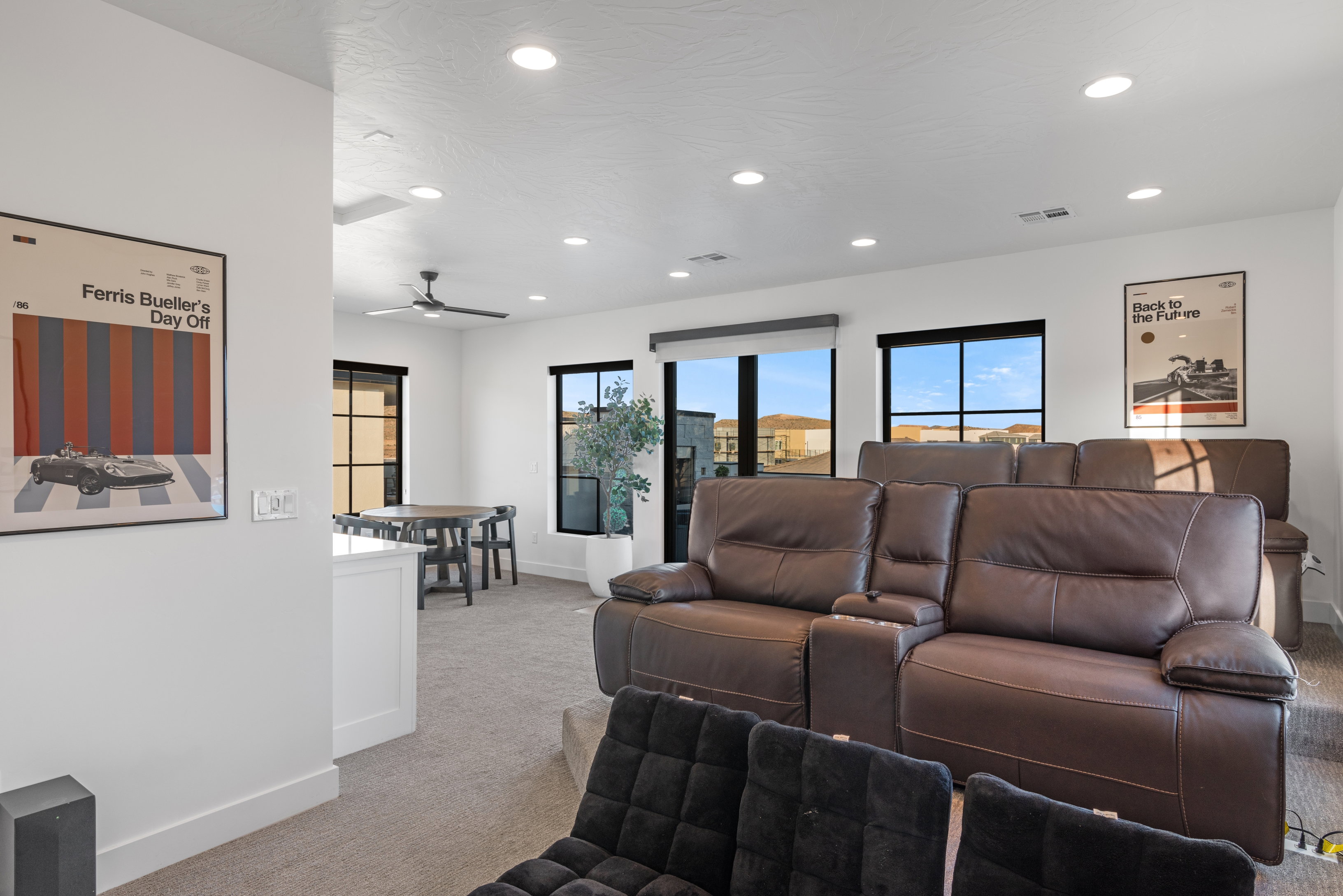 Spacious entertainment room featuring tiered seating, recessed lighting, large windows with black frames, and carpeted flooring