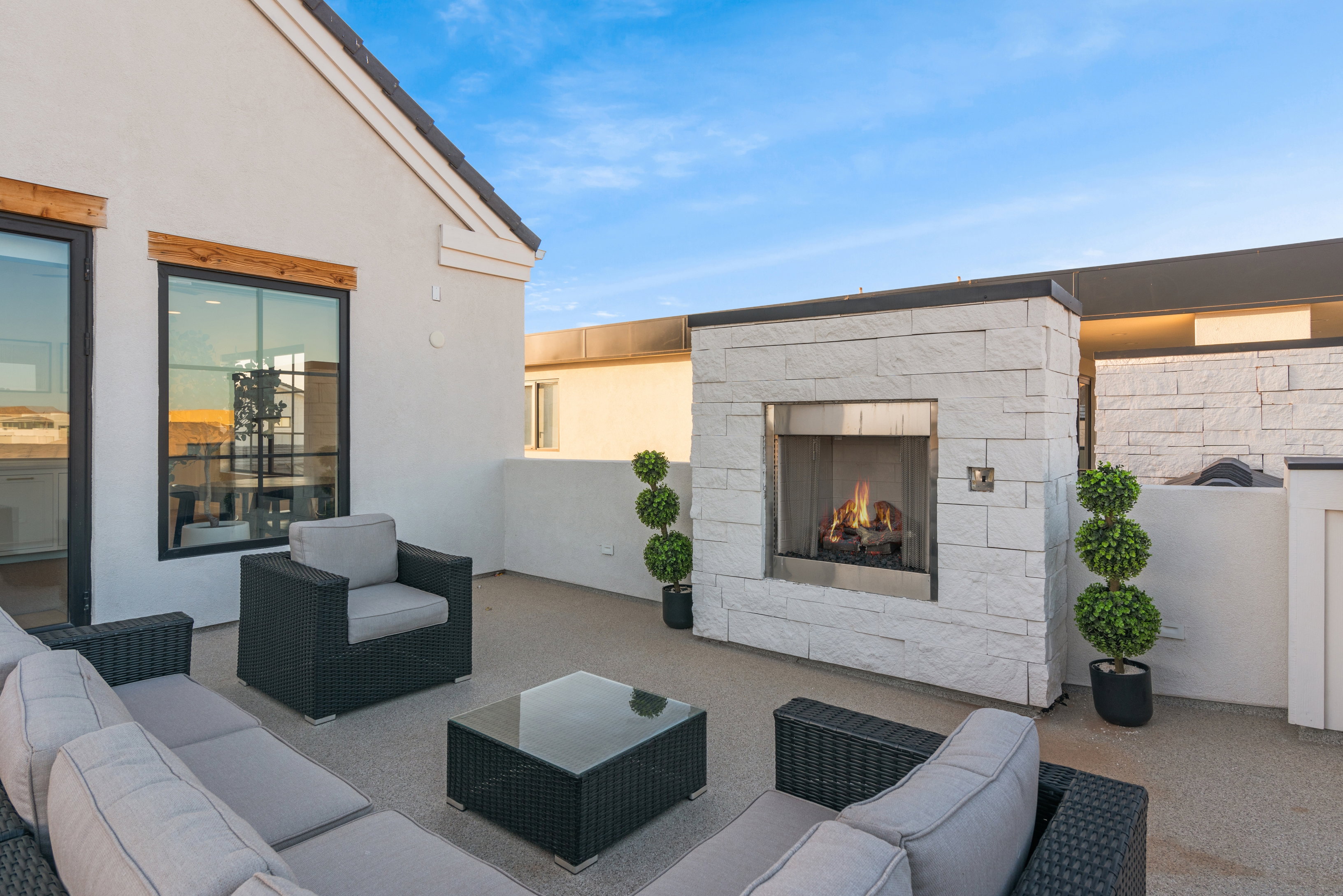 Rooftop patio featuring a stacked stone fireplace with stainless steel insert, light-toned textured stucco walls, and large black-framed windows with wood lintels